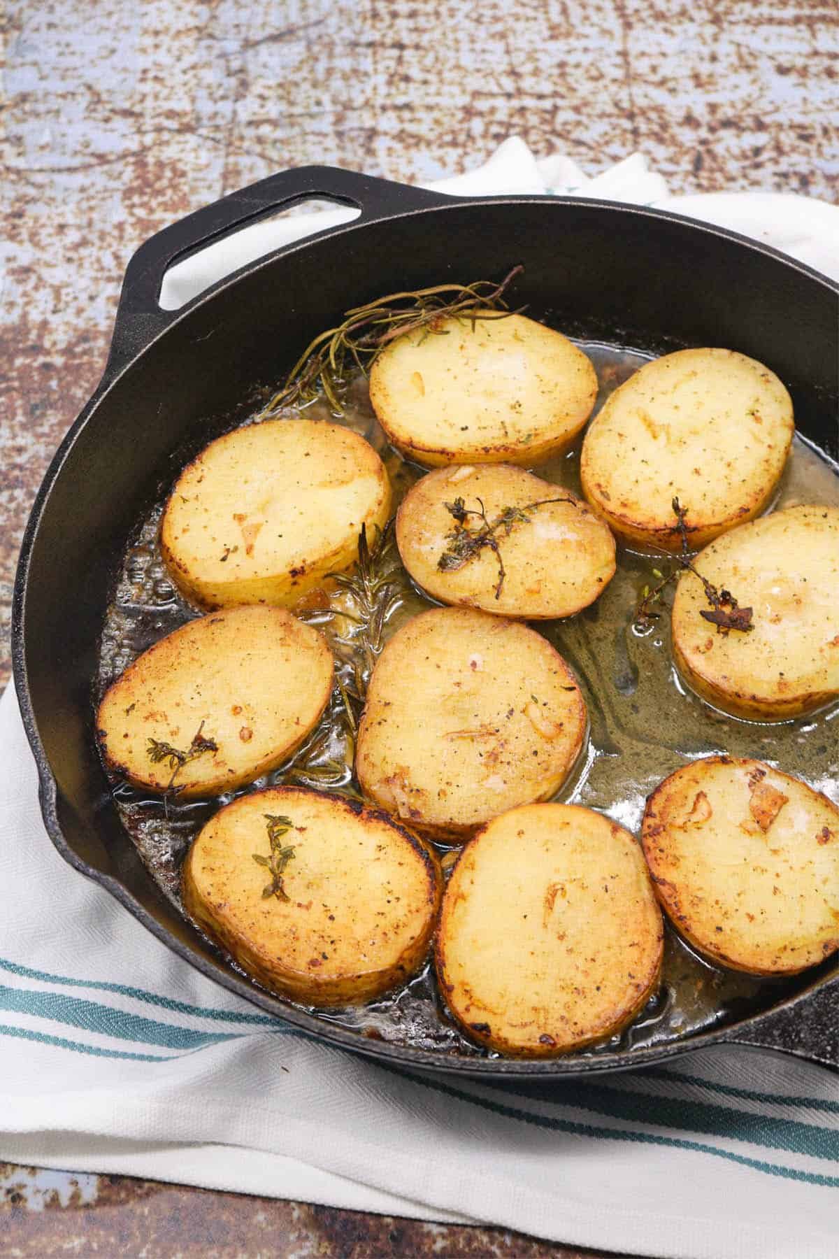 Buttery herbed melting potatoes in a skillet pan, sitting on a white and teal striped towel.