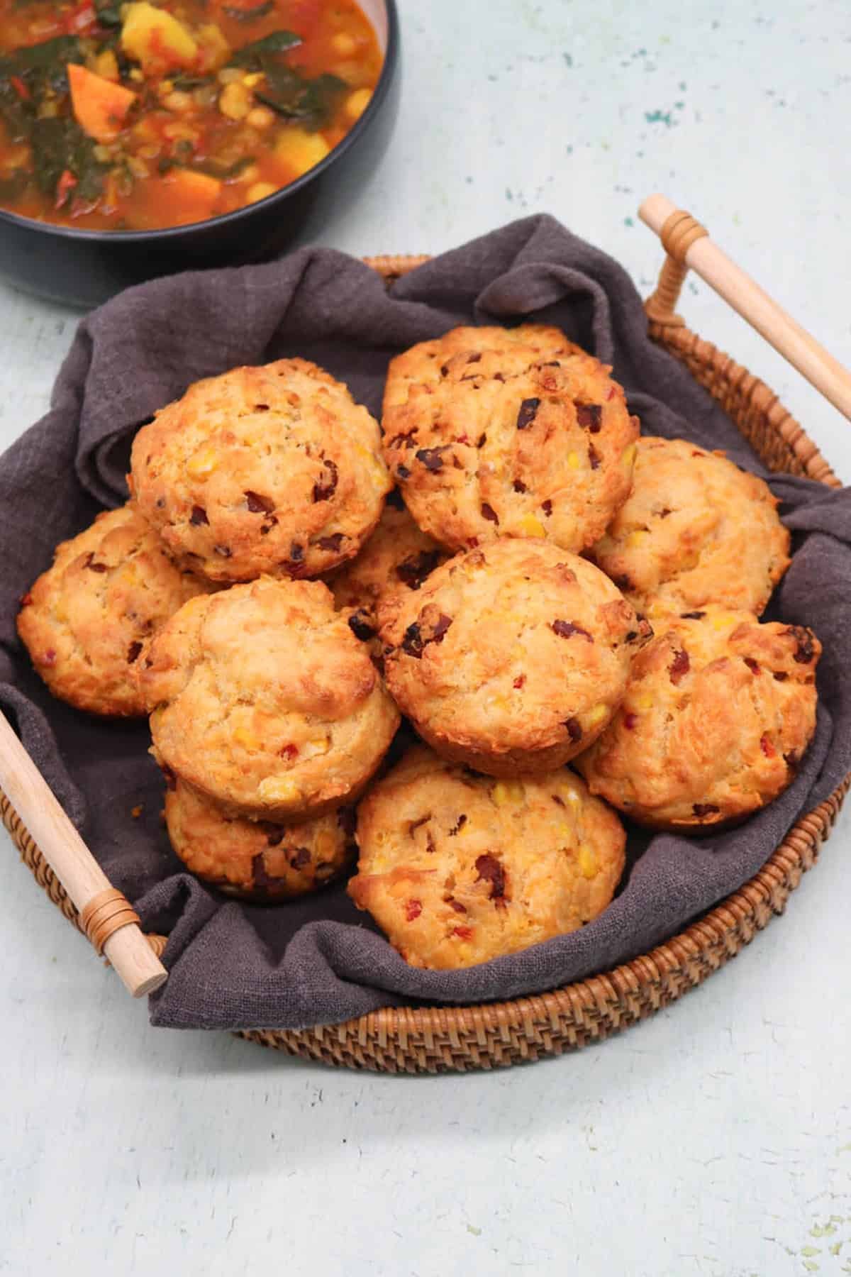 Chorizo, sweetcorn and chilli muffins in a bread basket, with a bowl of soup in the background.