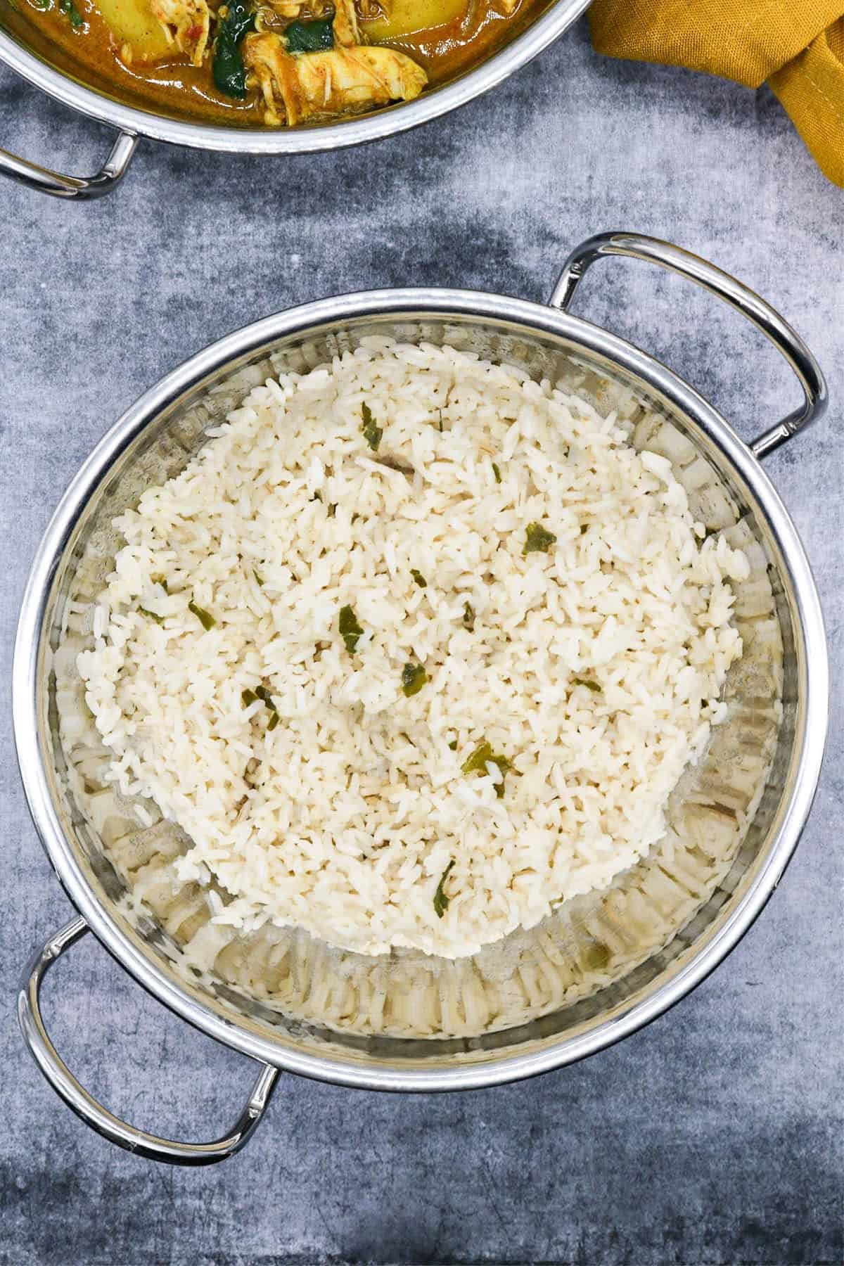 Coconut rice in a balti dish with a curry in another balti dish in the background.