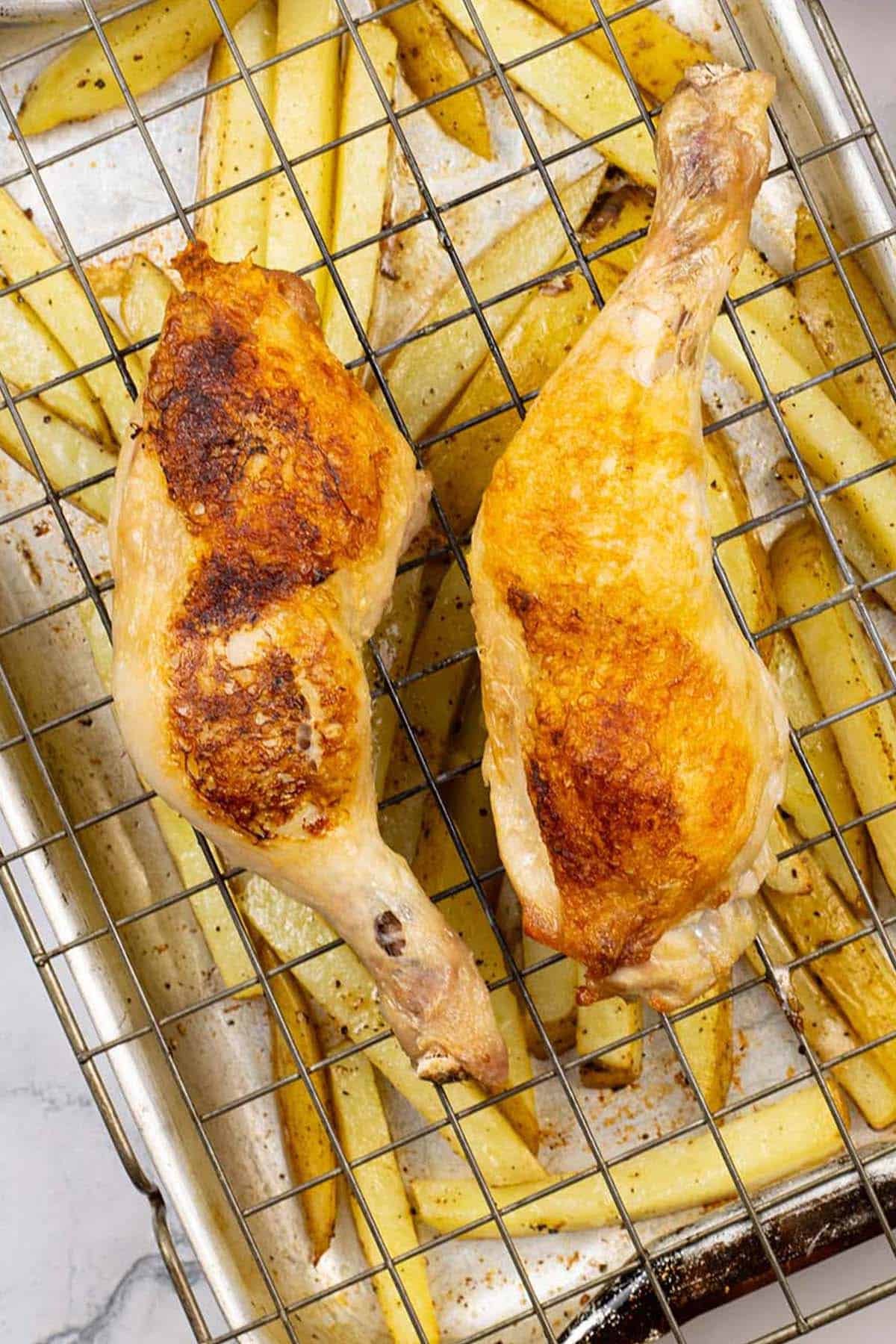 Close up photo of easy chicken legs and chips traybake in a roasting tin.