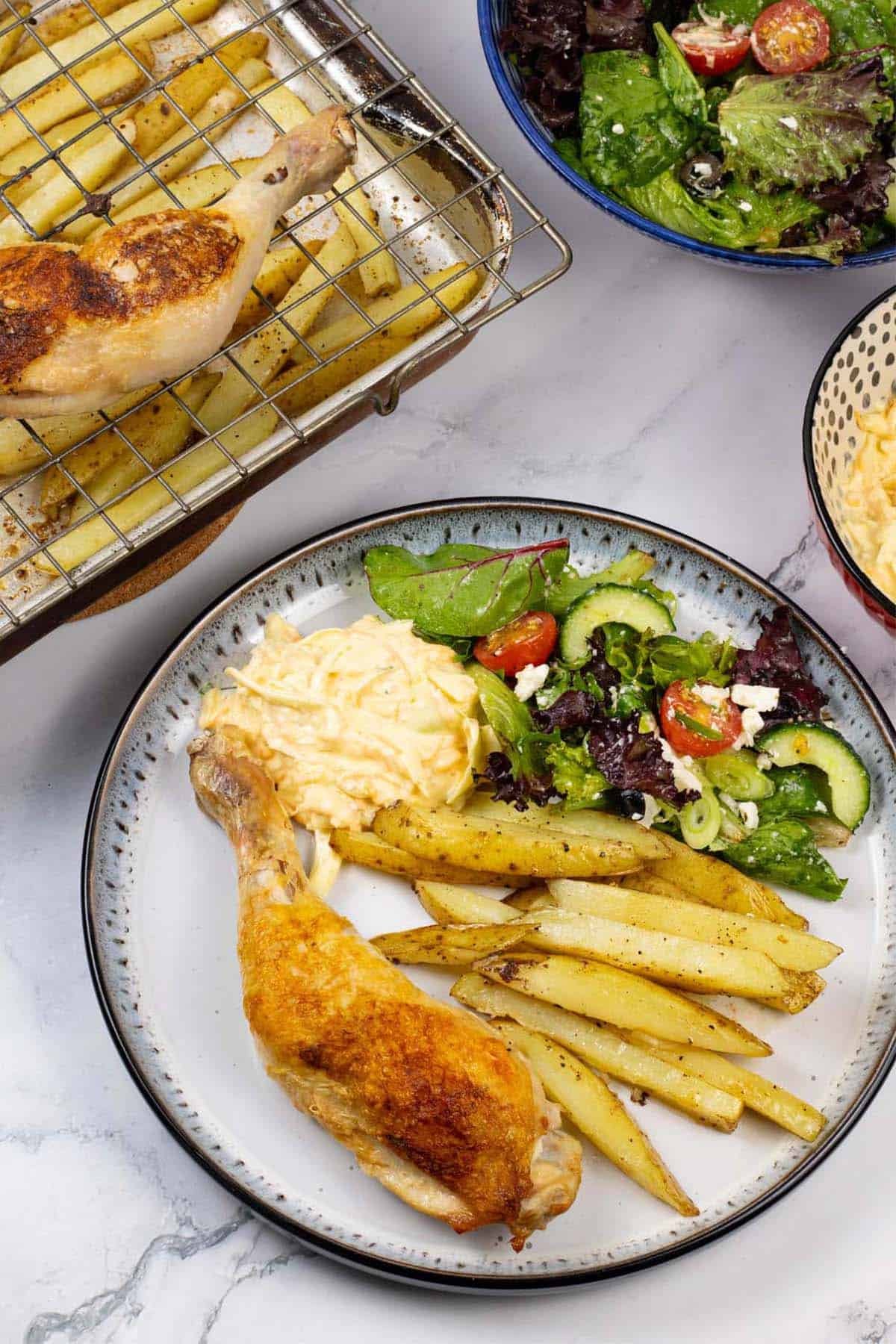 A portion of easy chicken legs and chips traybake plated with coleslaw and salad on the side.