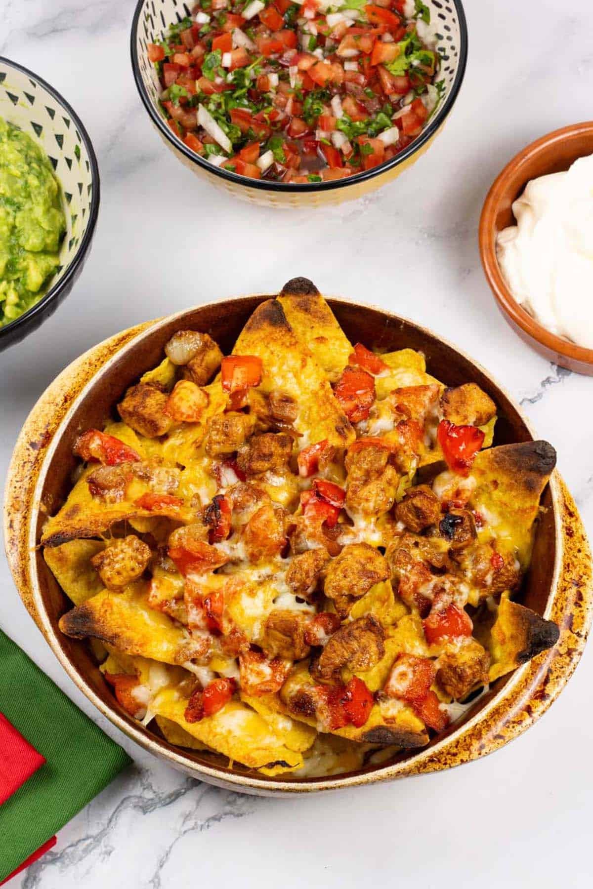 Smoky chicken fajita nachos in a stoneware dish with bowls of guacamole, pico de gallo salsa and sour cream on the side.