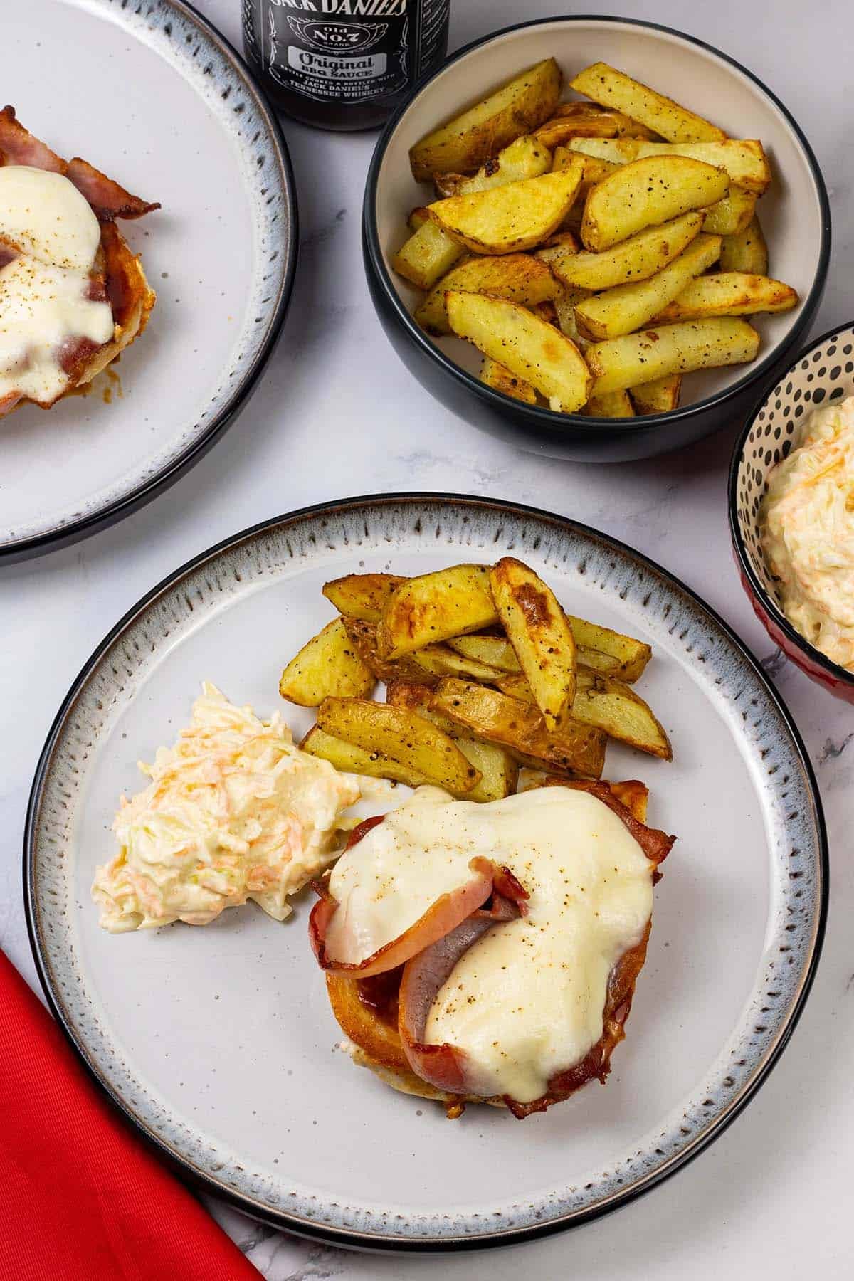 A portion of smothered chicken on a black and white dinner plate with coleslaw and chunky oven chips.