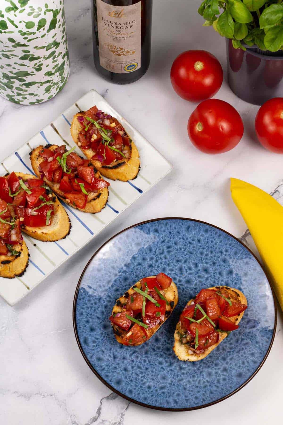 A portion of tomato bruschetta on a blue side plate with a striped platter of more bruschetta on the side.