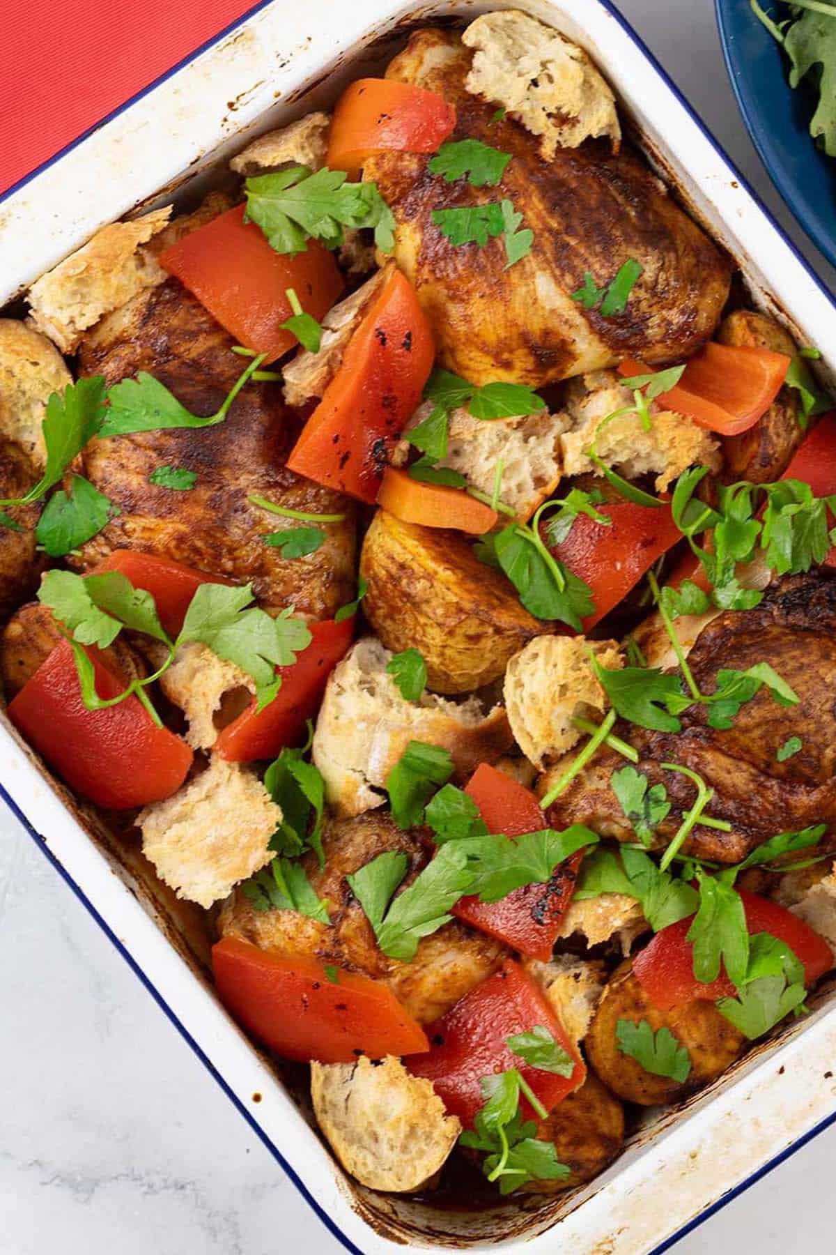 Chicken thighs with romesco traybake in a white enamel roasting tin.