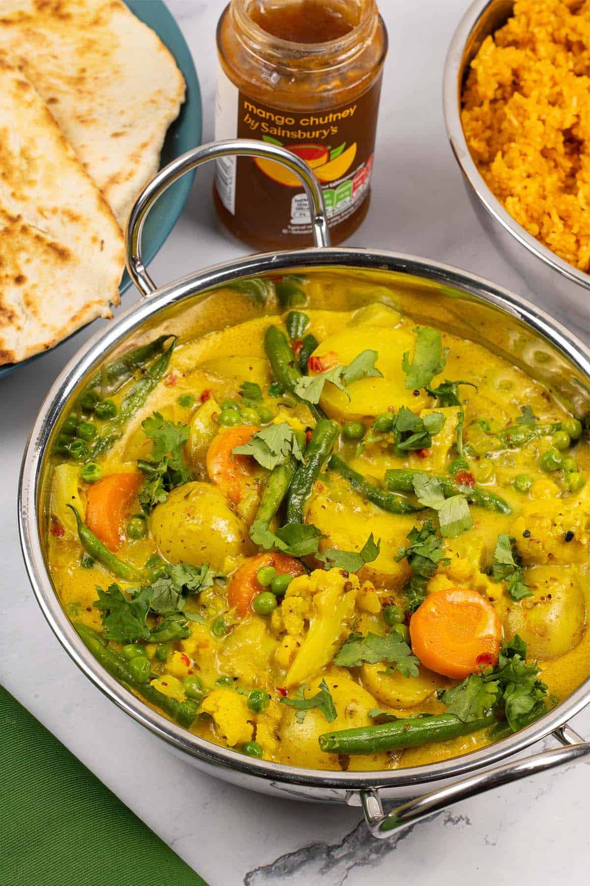 Easy Indian vegetable curry in a balti dish with red lentils and rice, mango chutney and quick naan breads in the background.