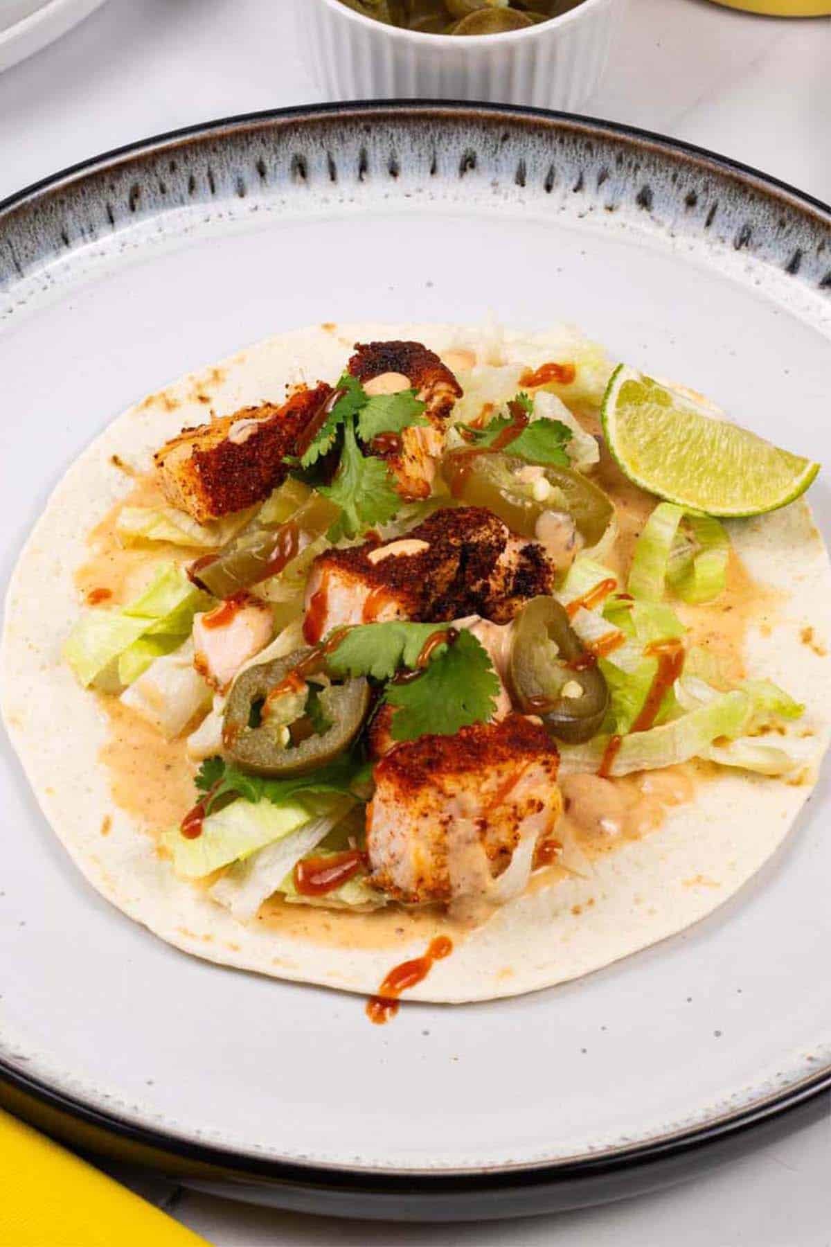 Grilled salmon tacos with chipotle lime yogurt on a white and black dinner plate.