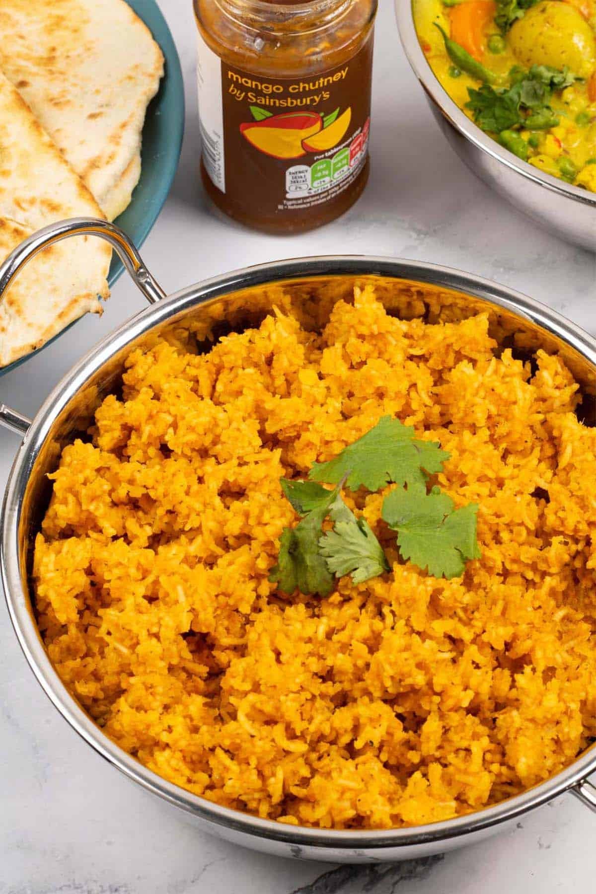 Red lentils and rice in a balti dish with quick naan breads, mango chutney and vegetable curry in the background.