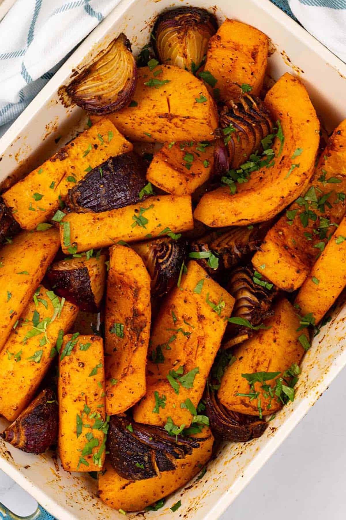 Roast paprika squash and red onions in a rectangle Staub ovenproof dish with a teal and white check towel.