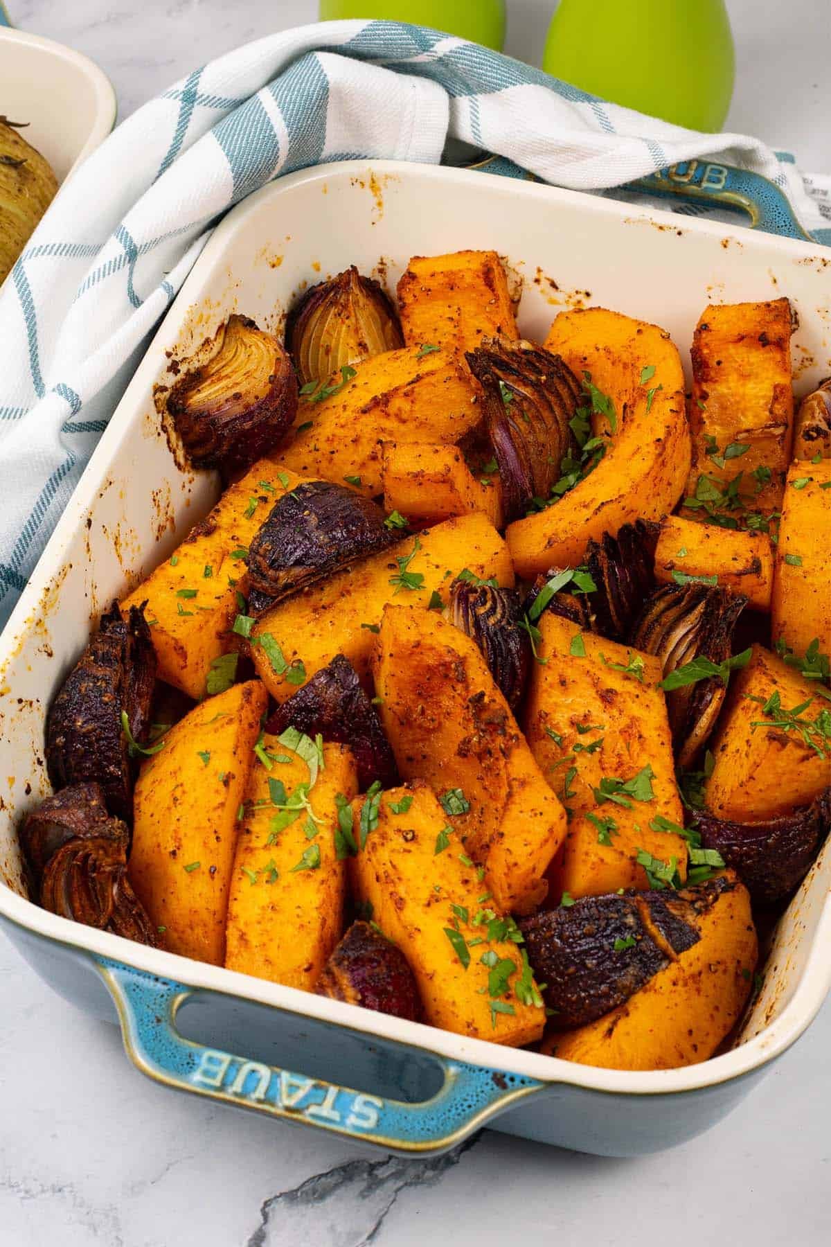 Roast paprika squash and red onions in a rectangle Staub ovenproof dish with a teal and white check towel.