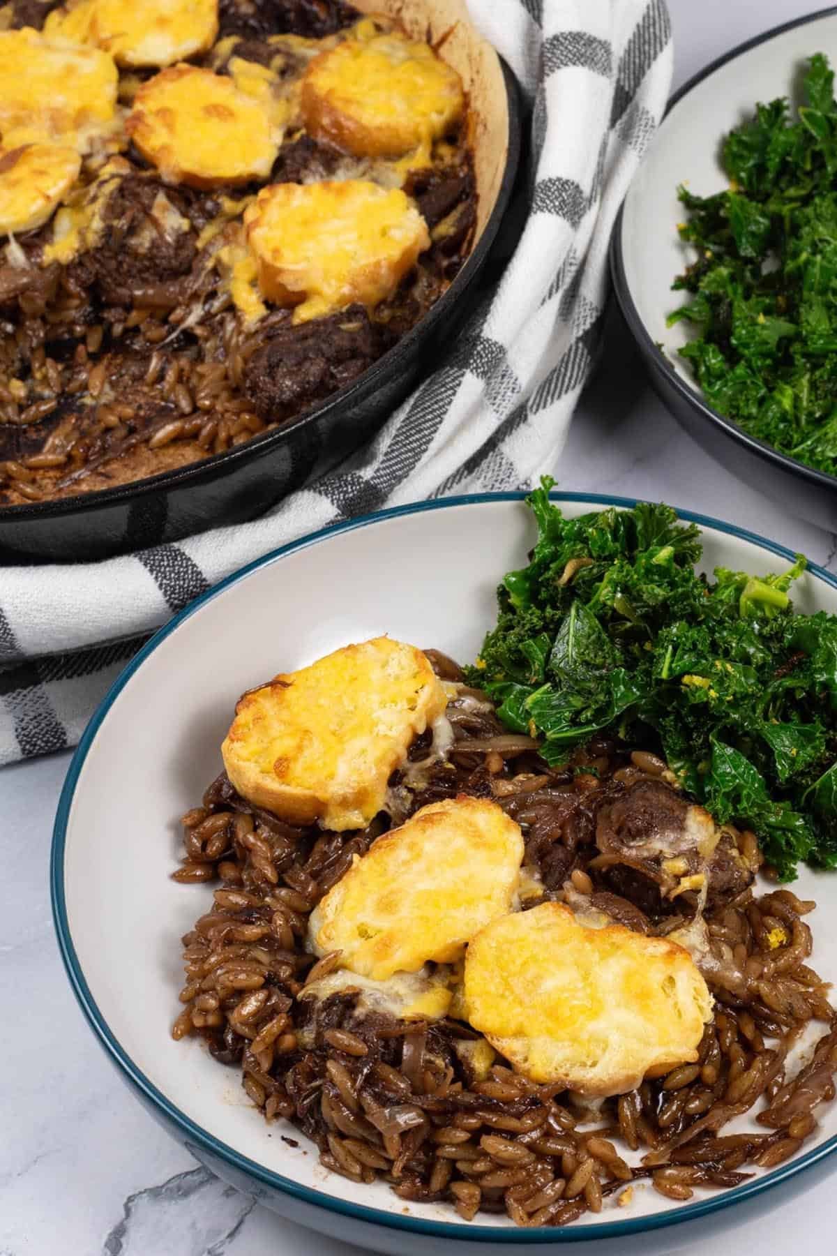 A bowl of french onion meatballs with orzo, with sautéed kale with chilli and lemon on the side.