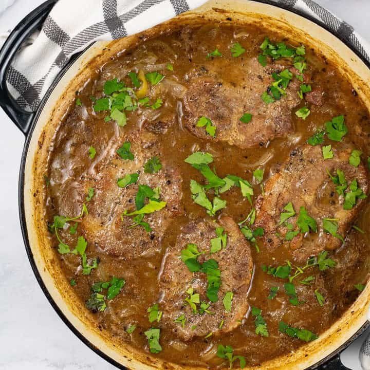 Cider braised pork steaks with onions in a large shallow round casserole.