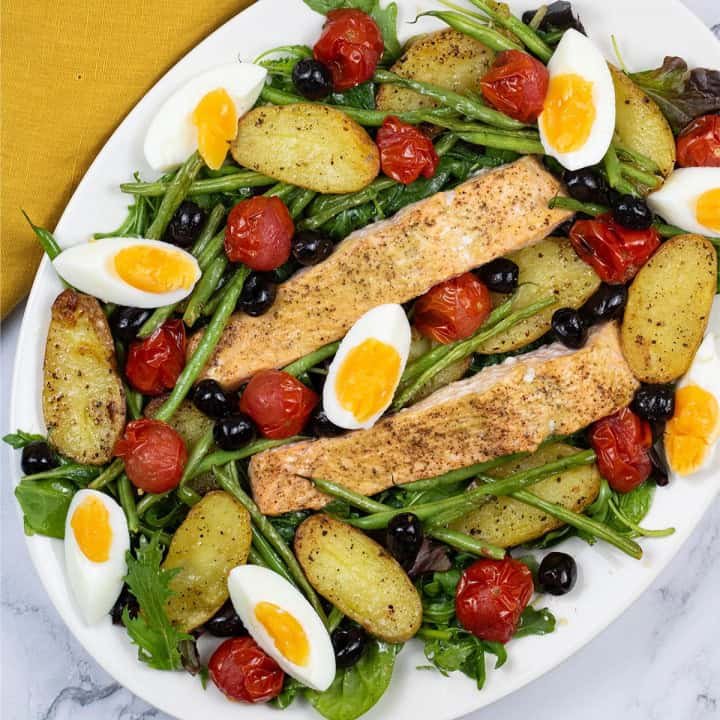 Easy salmon nicoise traybake on a white serving platter with a mustard napkin on the side.