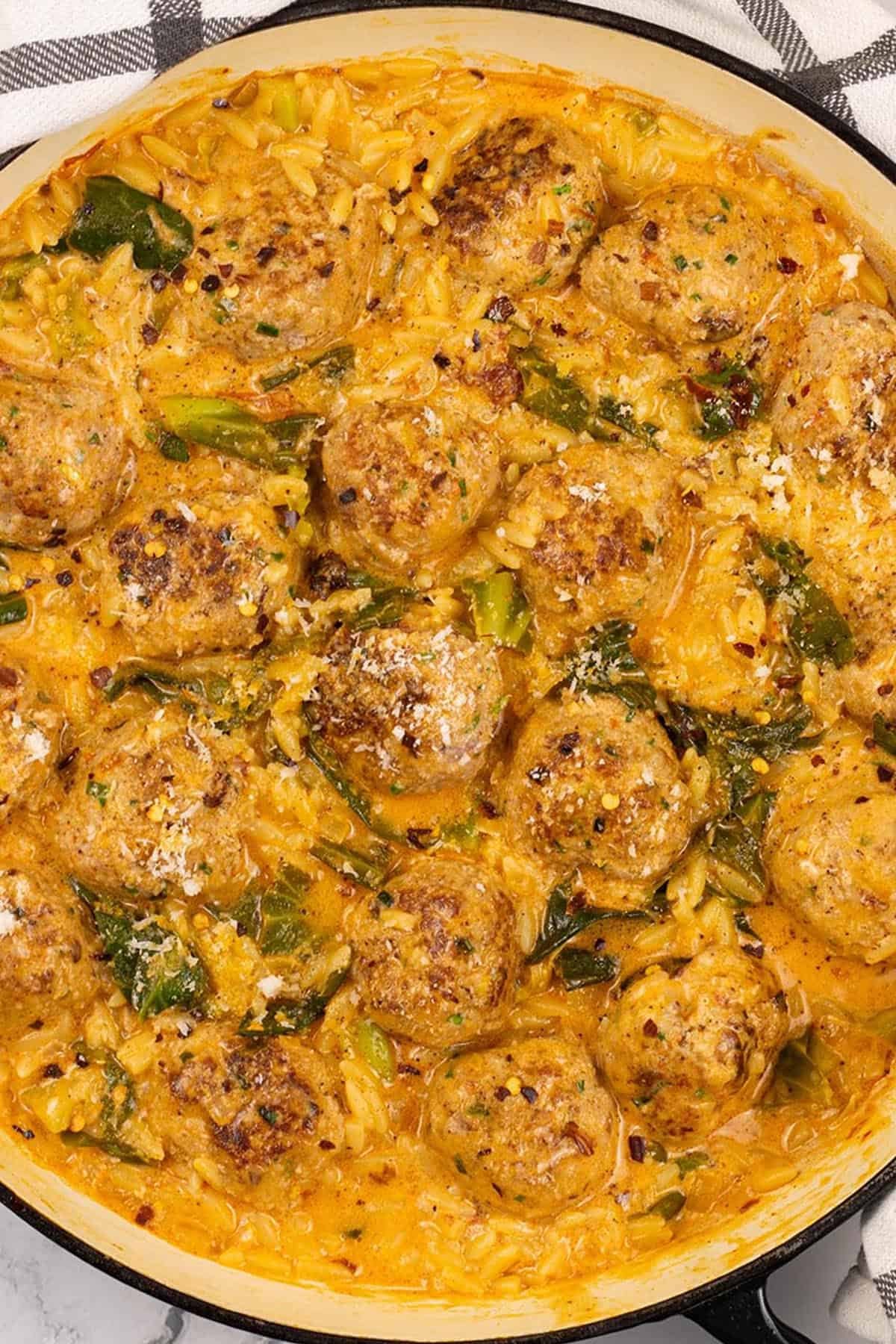 Marry me chicken meatball orzo in a large shallow casserole dish, with a black and white checked towel on the side.
