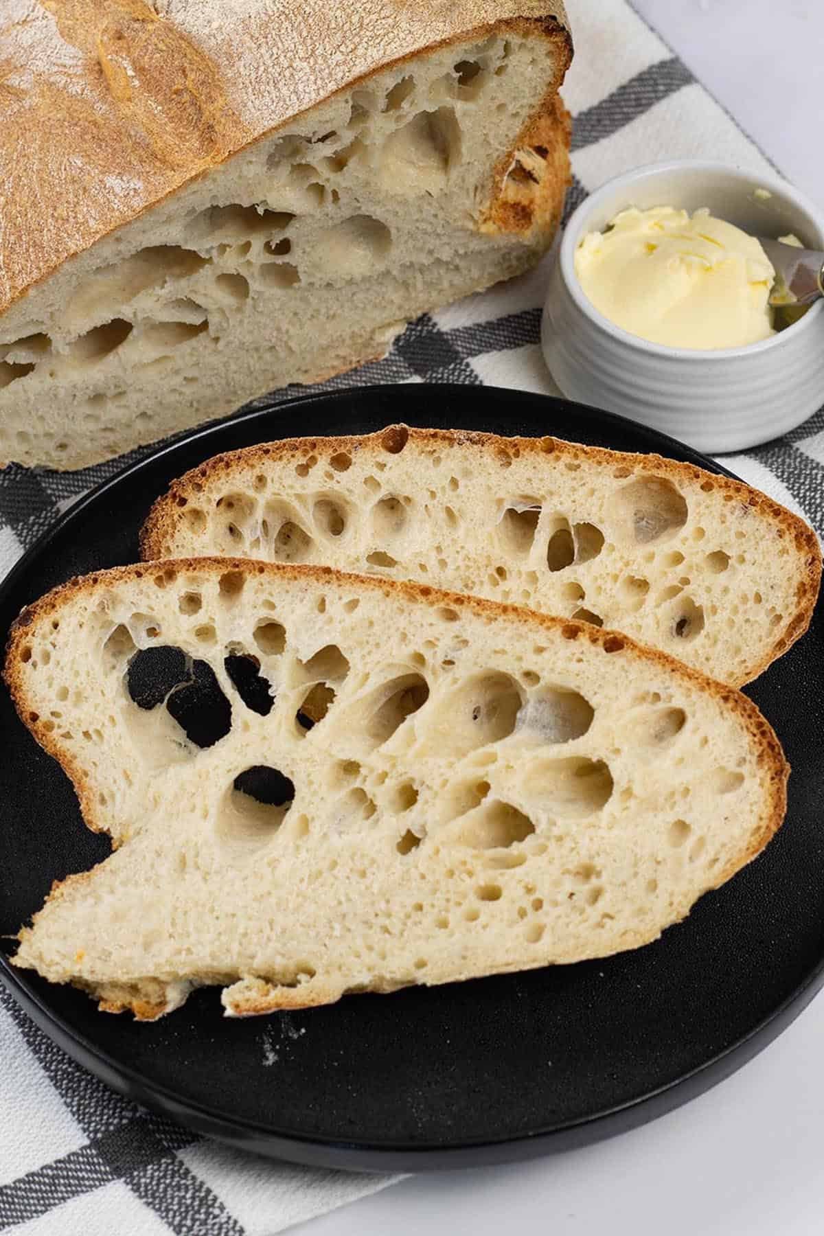 Portuguese water bread made in the Thermomix on a black and white checked towel, with a couple of slices on a black side plate.