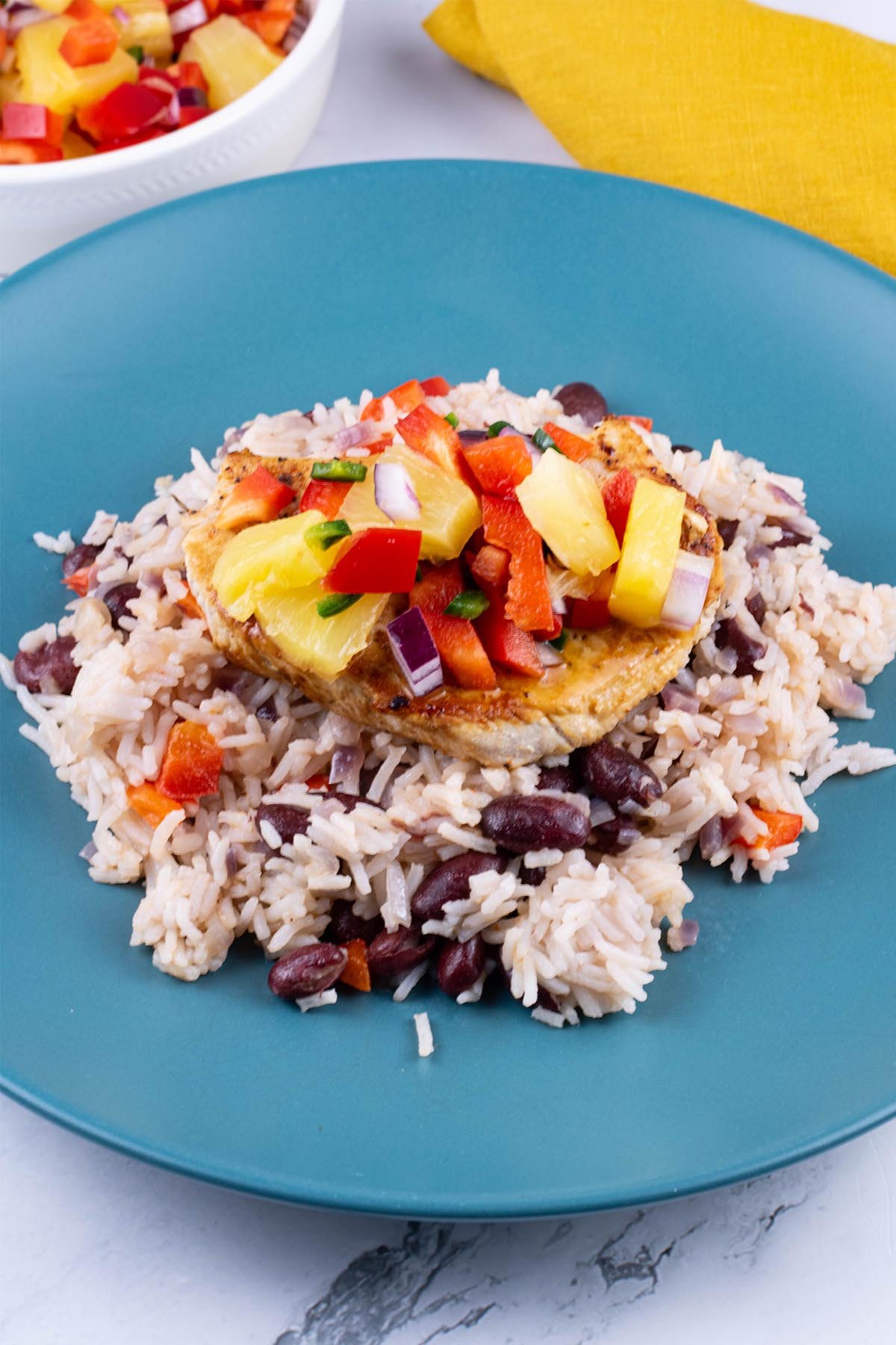 Cajun turkey steak with pineapple salsa and kidney bean rice on a teal plate. A bowl of salsa and mustard napkin on the side.