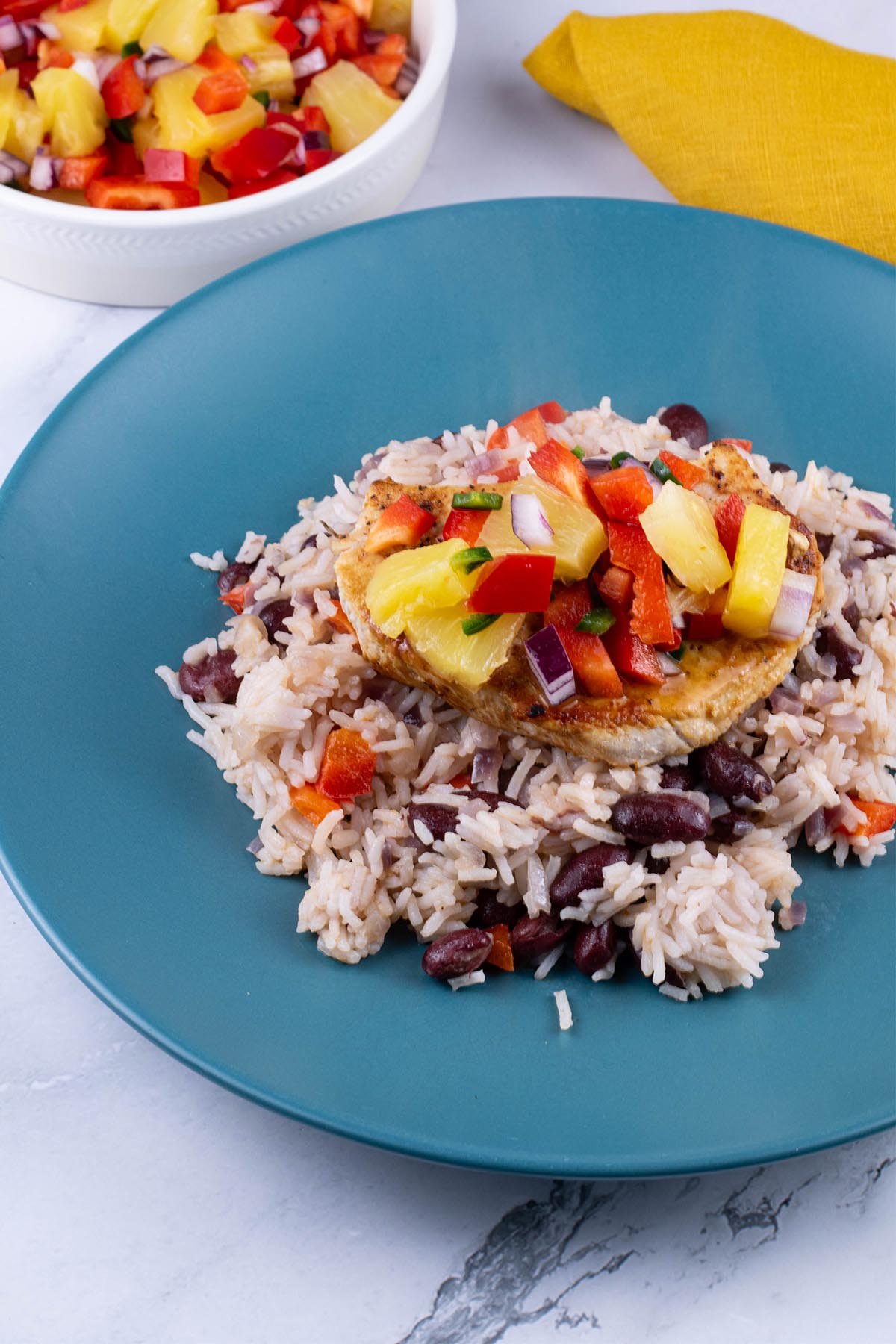 Cajun turkey steak with pineapple salsa and kidney bean rice on a teal plate. A bowl of salsa and mustard napkin on the side.