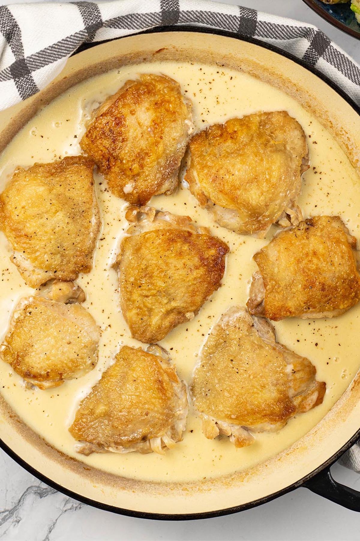 Cider braised chicken thighs in a large round shallow casserole.