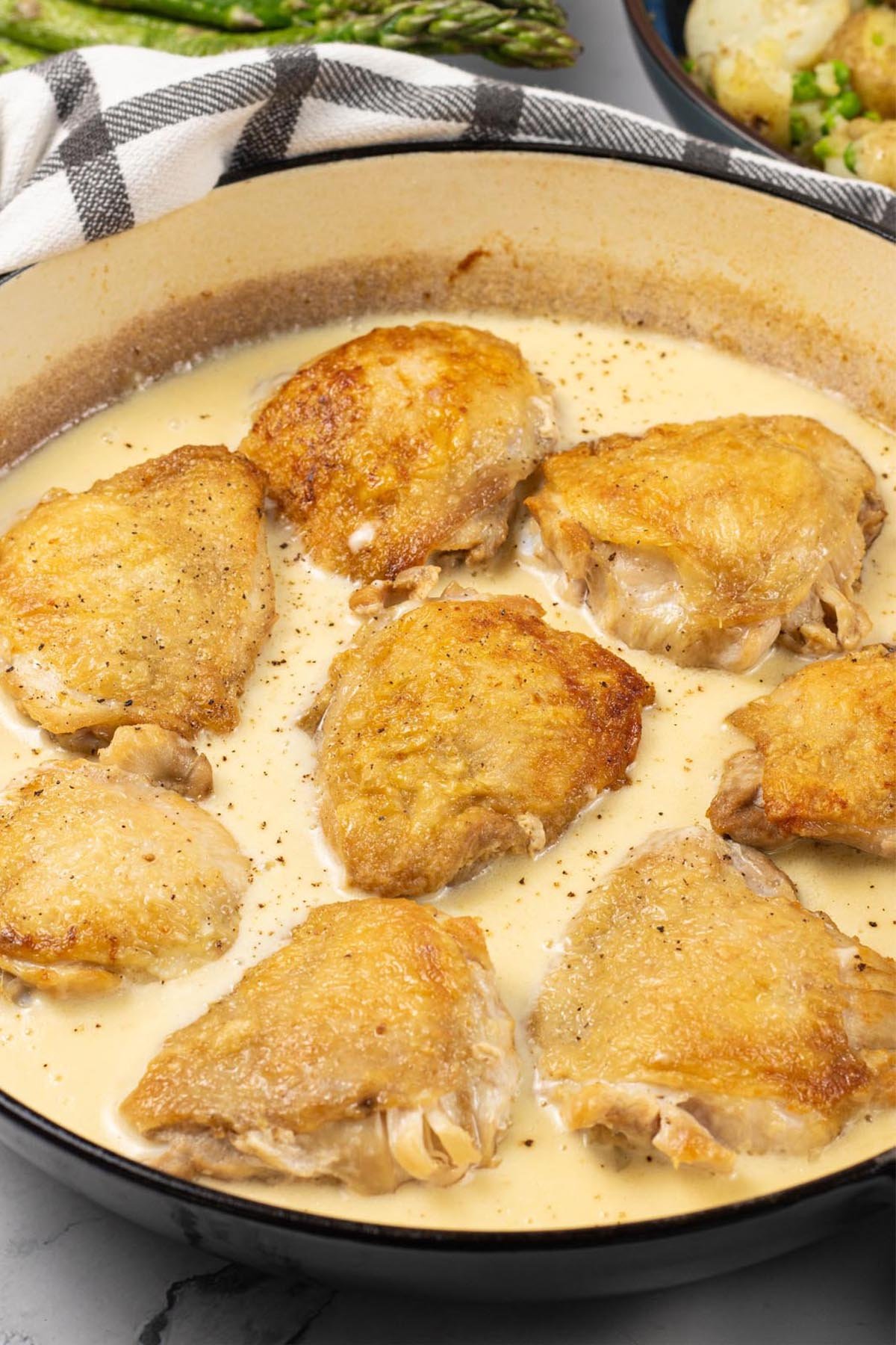 Cider braised chicken thighs in a large round shallow casserole.