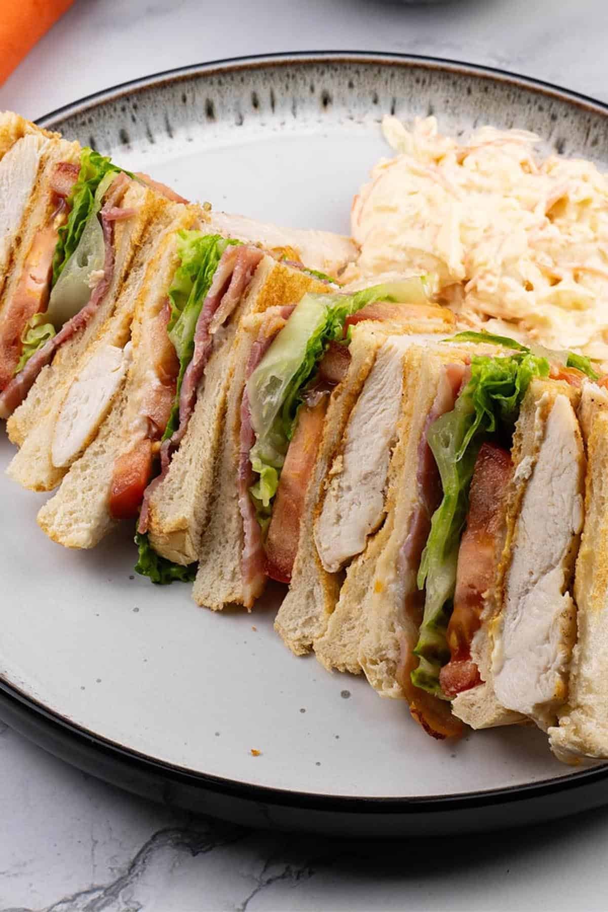 A club sandwich and coleslaw on a black and white patterned dinner plate.