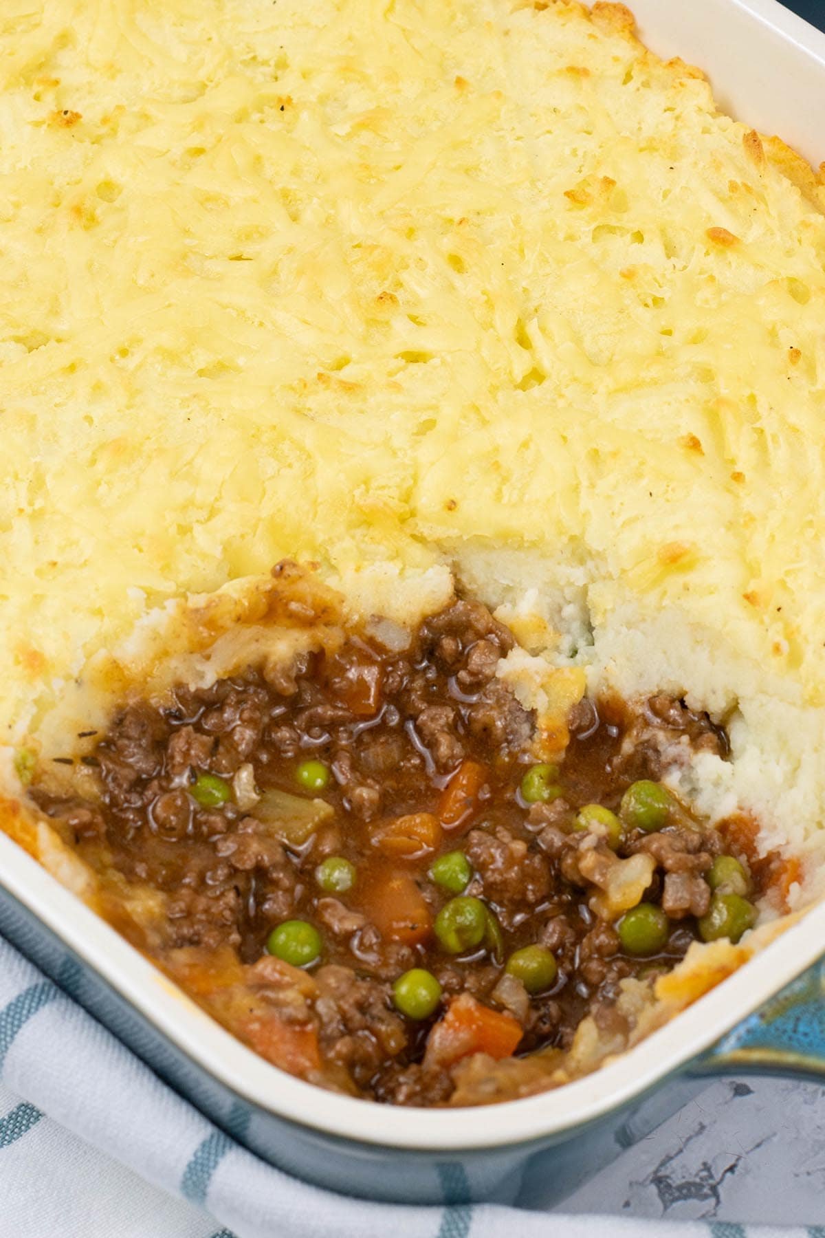 Close up photo of cottage pie in a rectangle oven dish with a portion of potato topping removed.