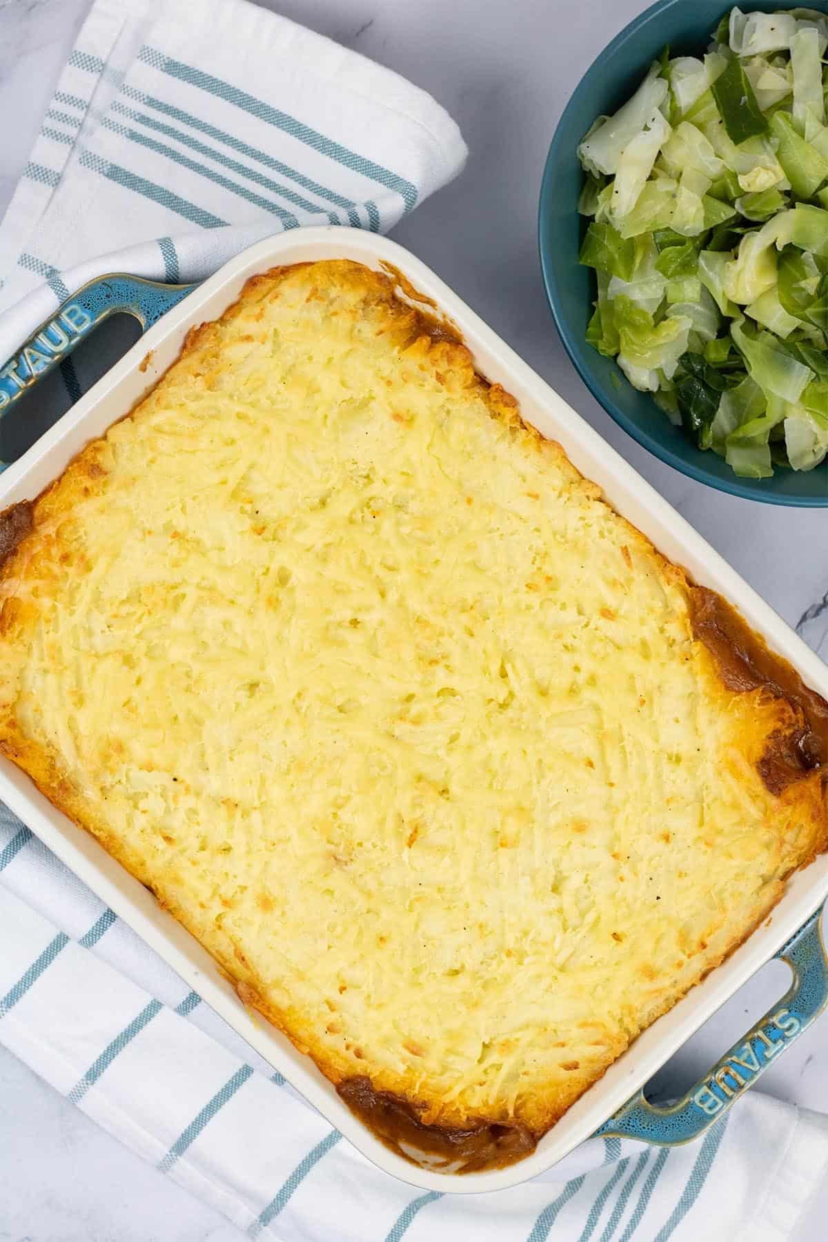 Cottage pie in a rectangle oven dish with a bowl of cabbage on the side.