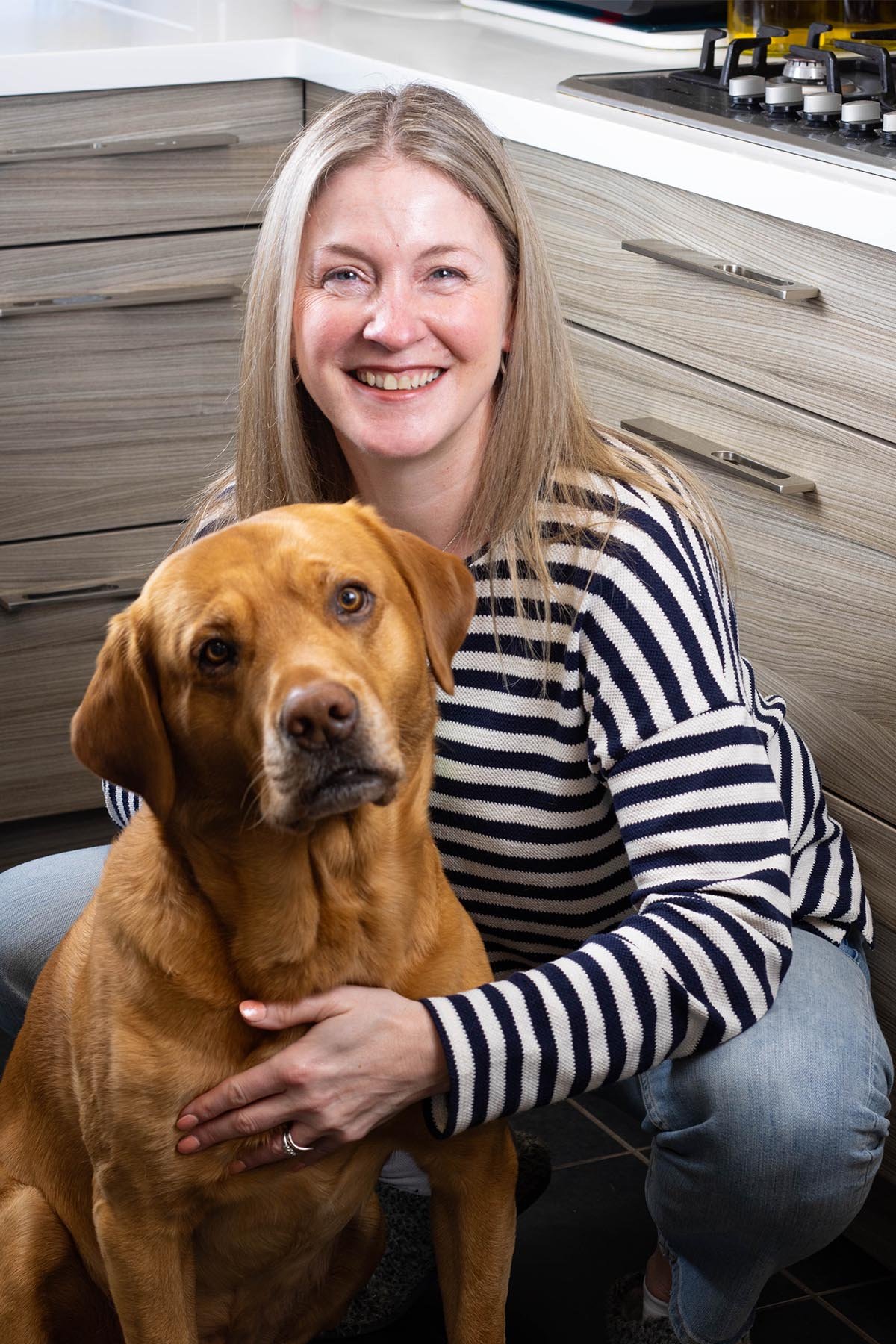 Deborah crouched down in kitchen with their 6 year old fox red labrador Ritchie.