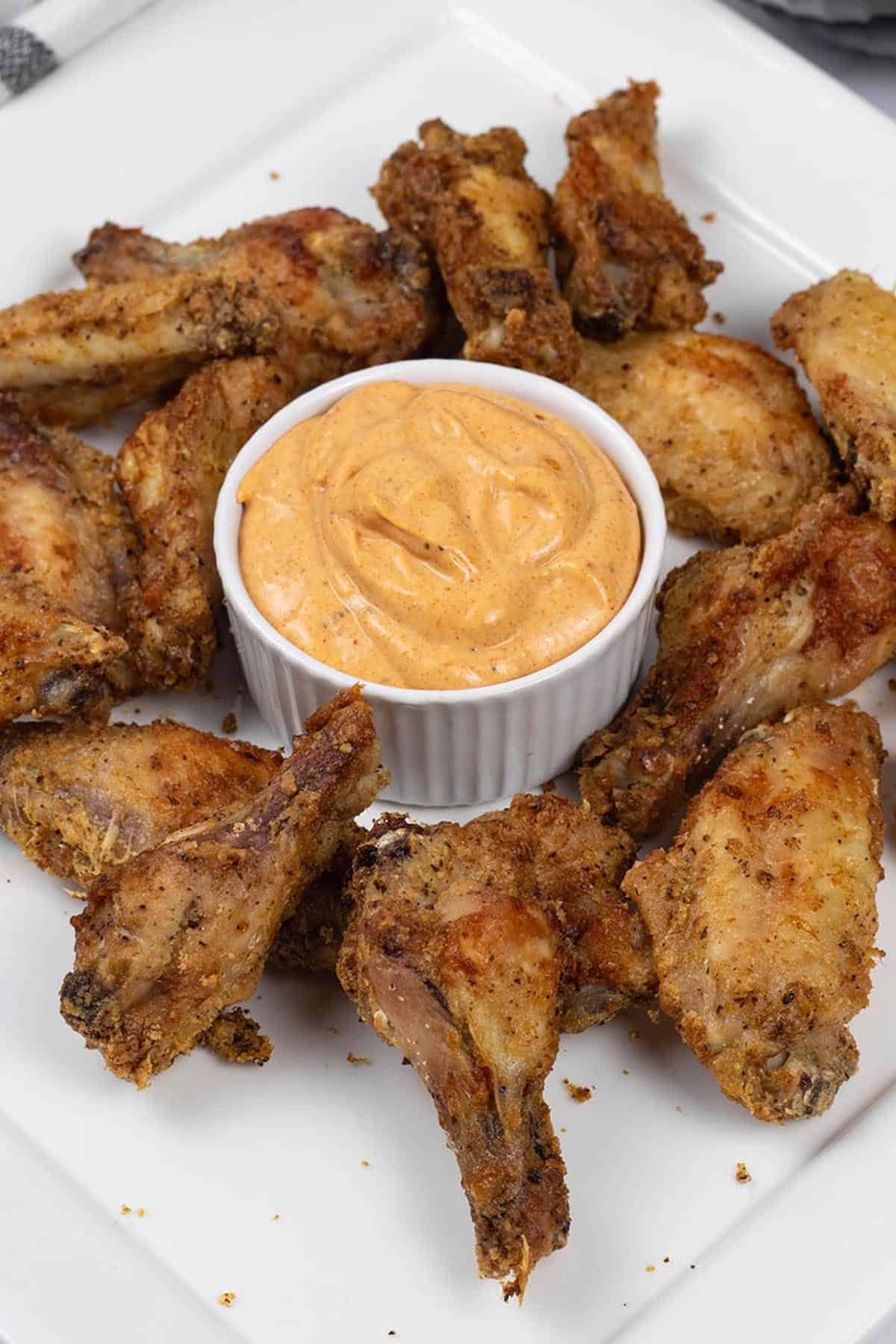 Easy air fryer cajun chicken wings on a white square platter with a dish of cajun dipping sauce.