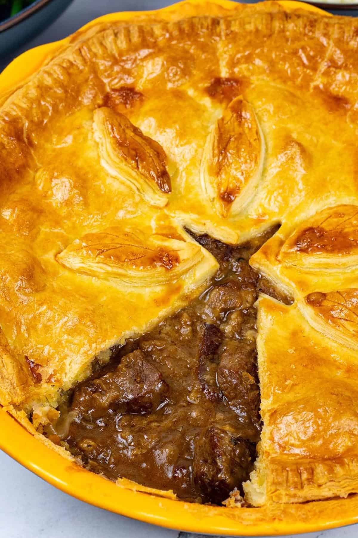 Easy steak pie in a round yellow pie dish with a triangle of pastry cut out.