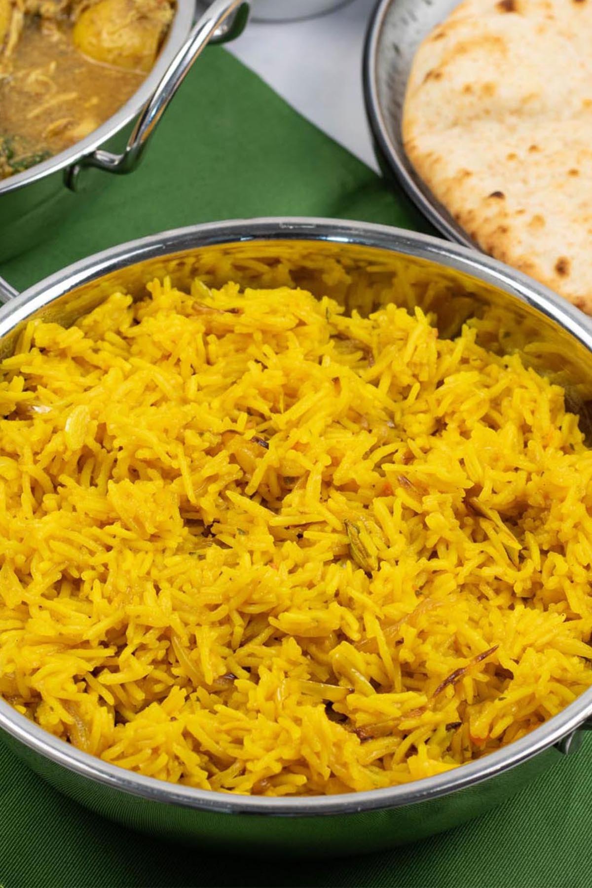 Golden pilau rice in a balti dish with a dish of slow cooker chicken and potato curry, and plate of chapatis in the background.