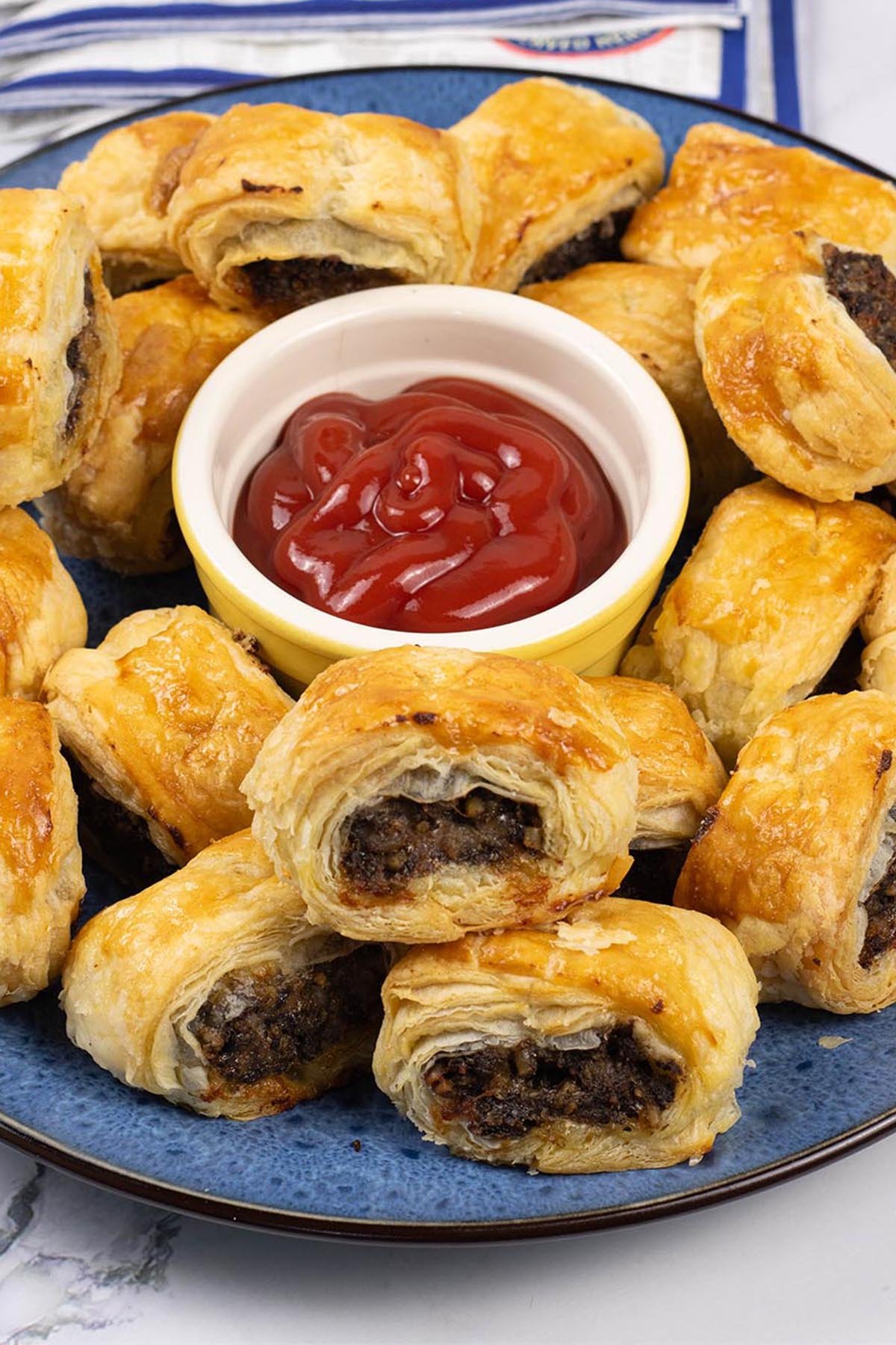 Haggis and pork sausage rolls on a blue patterned serving plate with a small dish of tomato ketchup in the centre.
