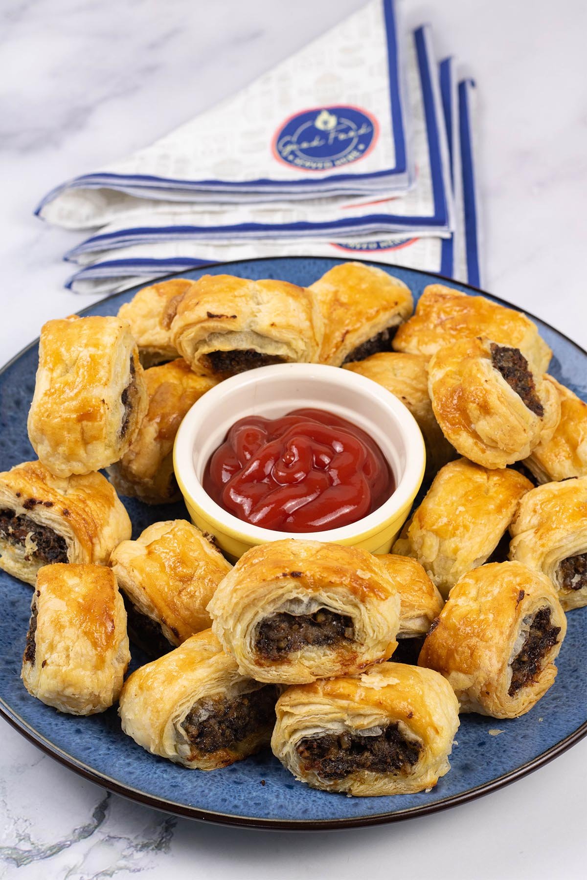 Haggis and pork sausage rolls on a blue patterned serving plate with a small dish of tomato ketchup in the centre.