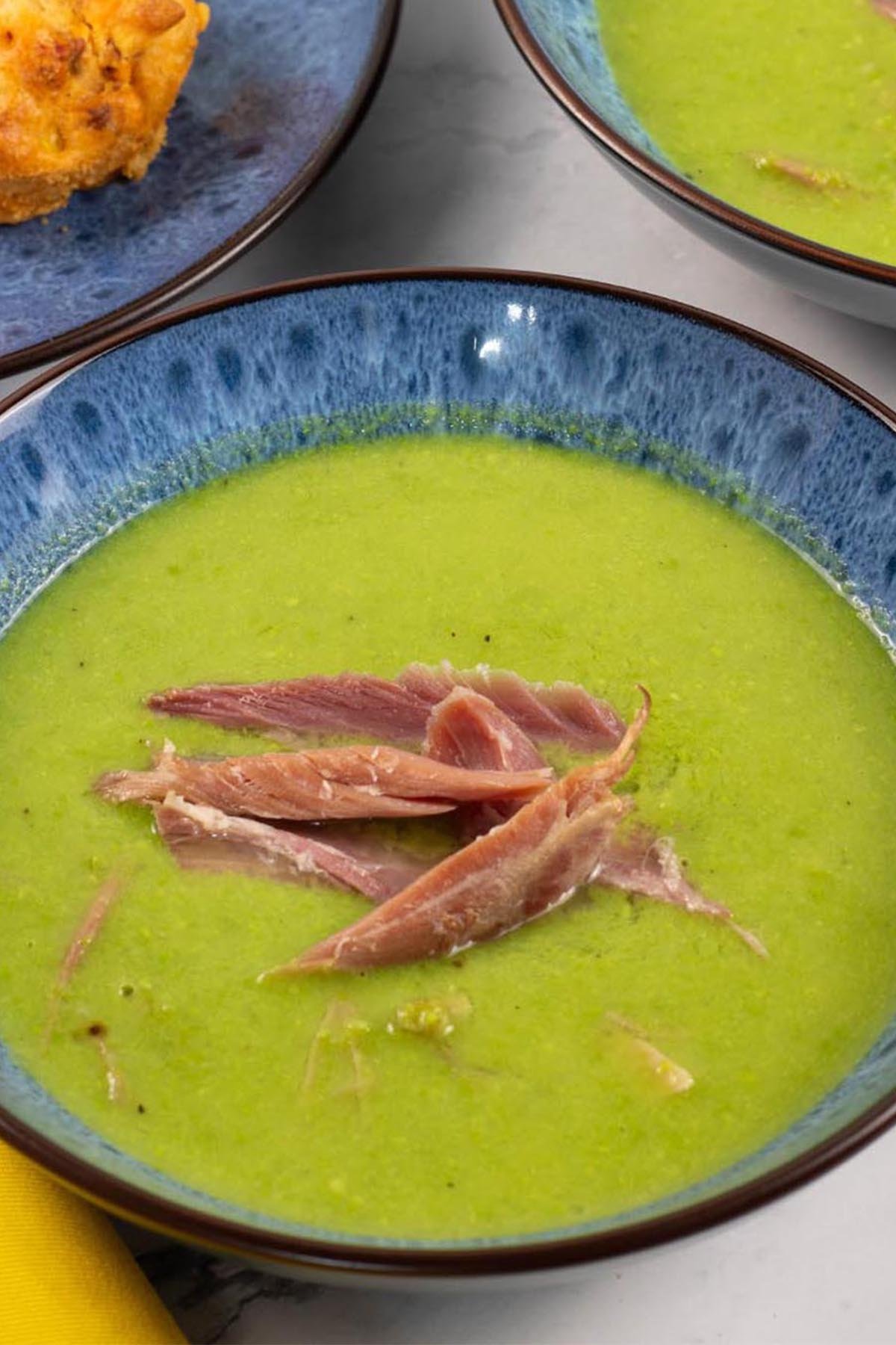 Two portions of pea and ham soup in blue patterned bowls with a plate of chorizo, sweetcorn and chilli muffins on the side.