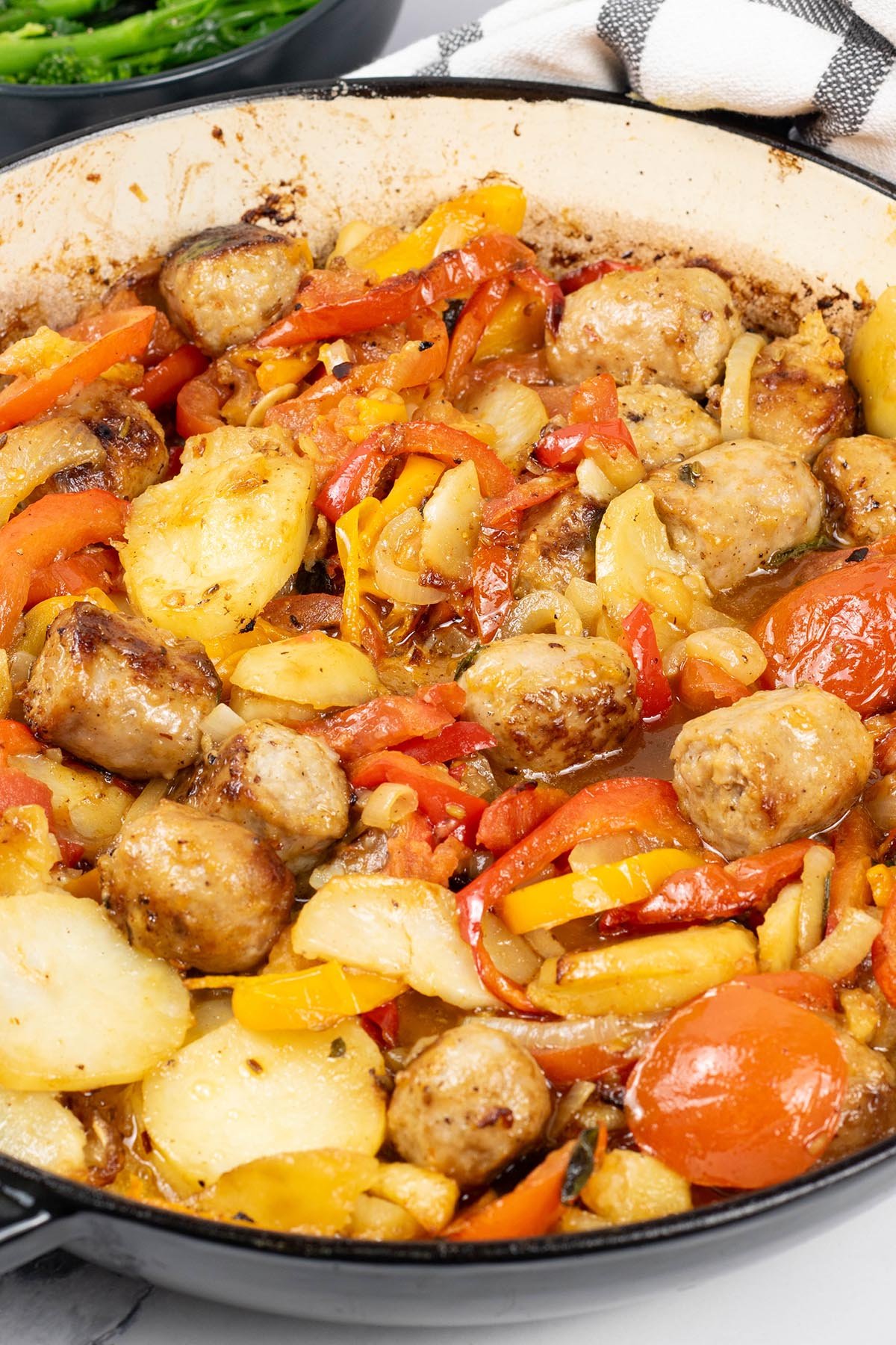 Close up photo of salsiccia con patate e pomodori al forno in a large round casserole.