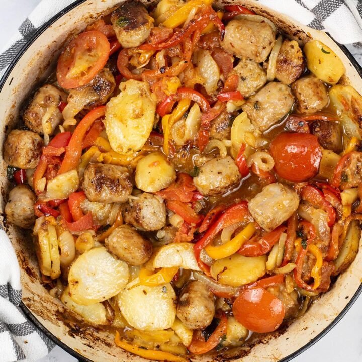 Salsiccia con patate e pomodori al forno in a large round casserole.