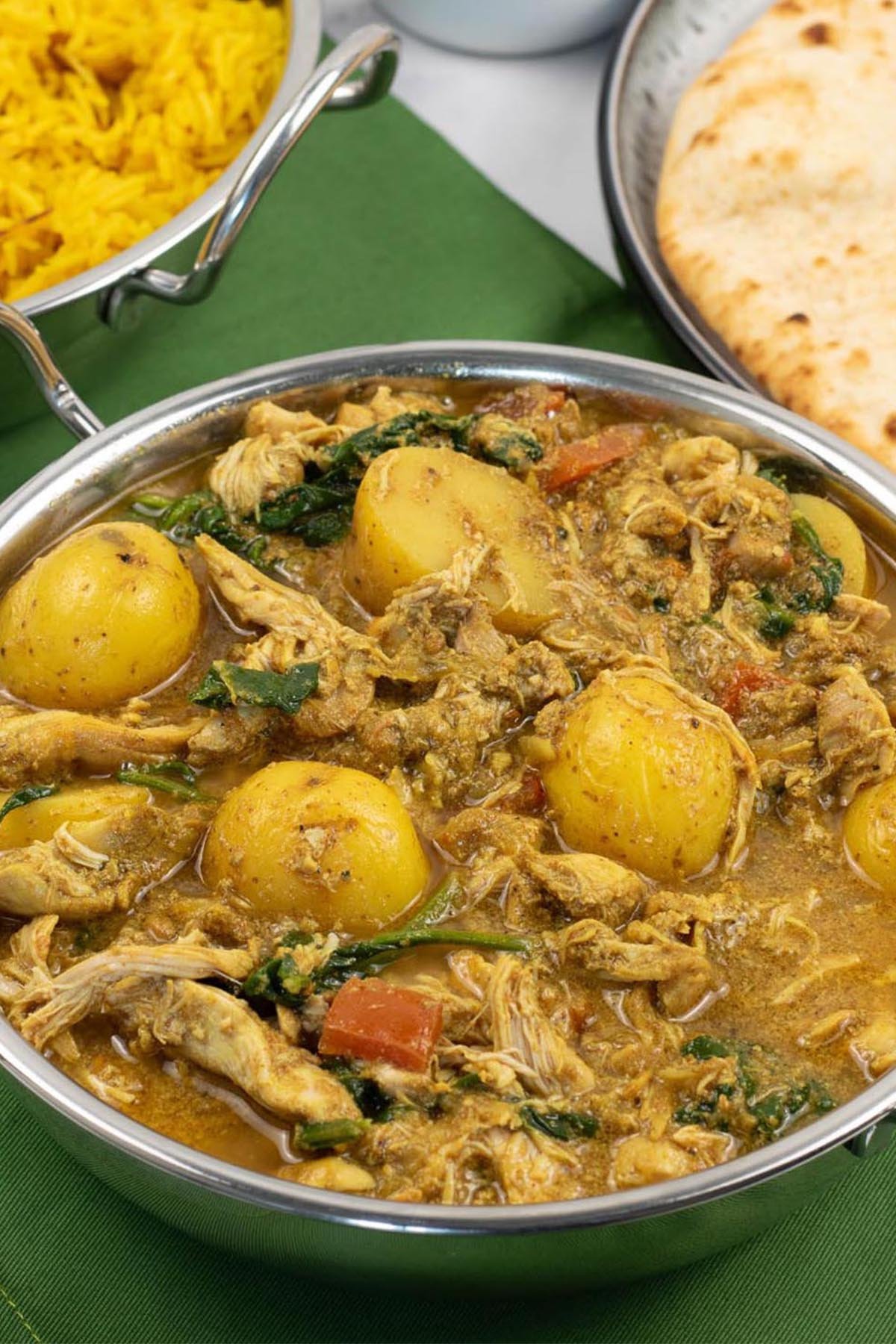 Slow cooker chicken and potato curry in a balti dish with golden pilau rice and chapatis in the background.