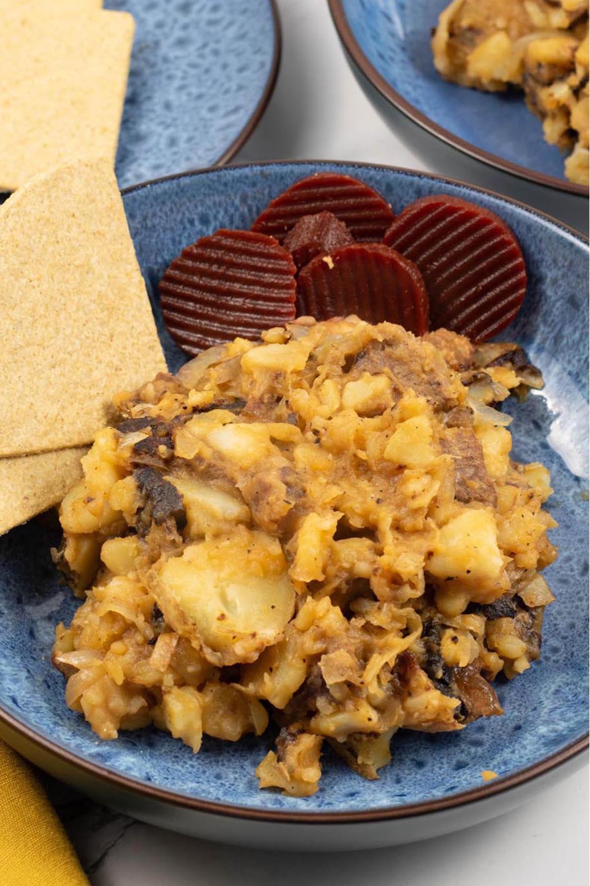 Two portions of stovies in blue patterned bowls, garnished with sliced beetroot and oatcakes.