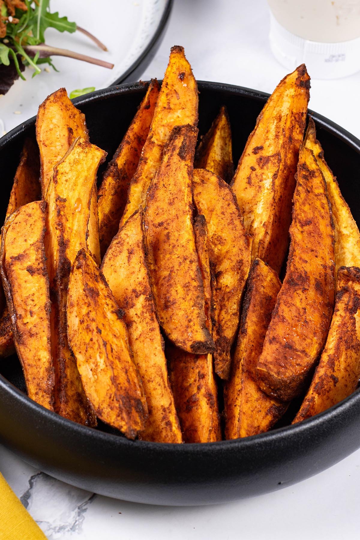 Close up photo of sweet potato wedges in a black serving bowl.