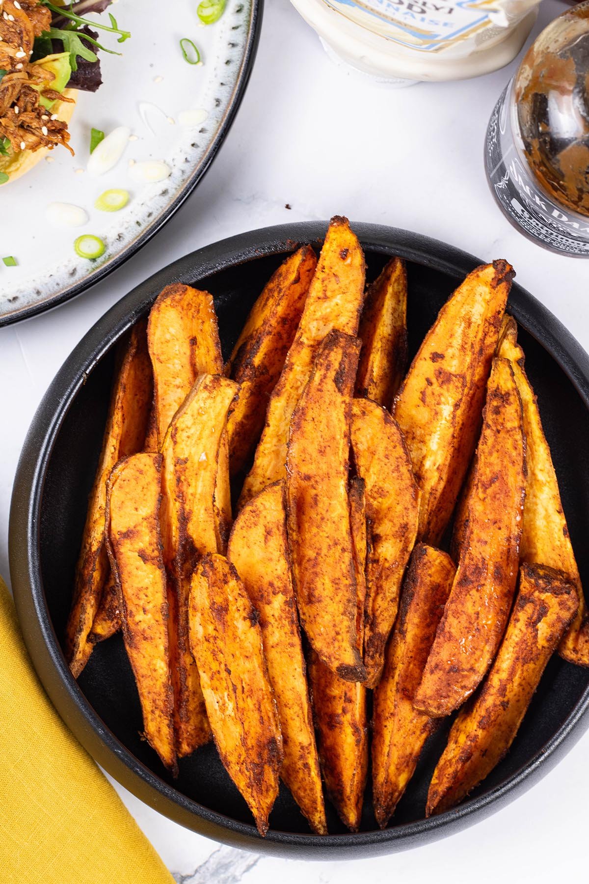 Sweet potato wedges in a black serving bowl with a mustard napkin on the side.