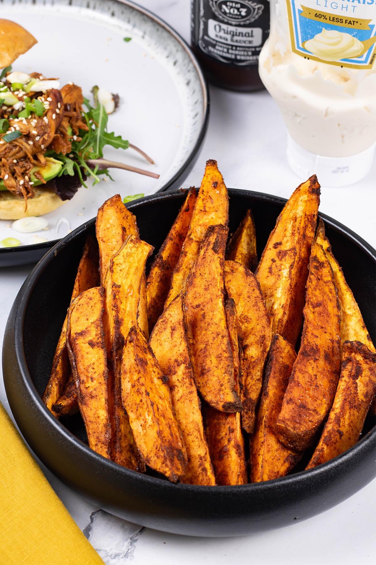 Sweet potato wedges in a black serving bowl with a mustard napkin on the side.