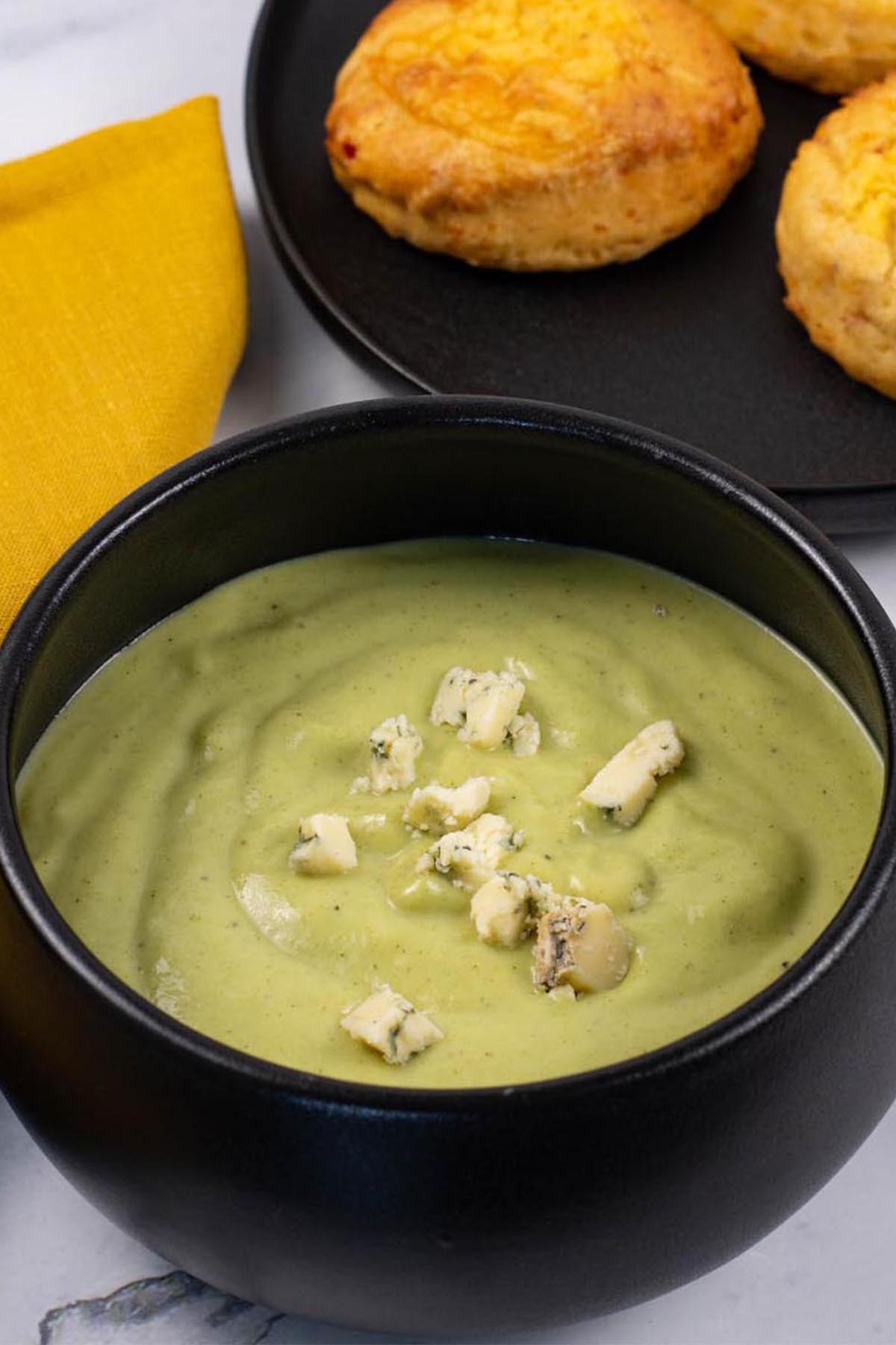 A portion of broccoli and stilton soup garnished with crumbled stilton in a black bowl, made in the Thermomix.