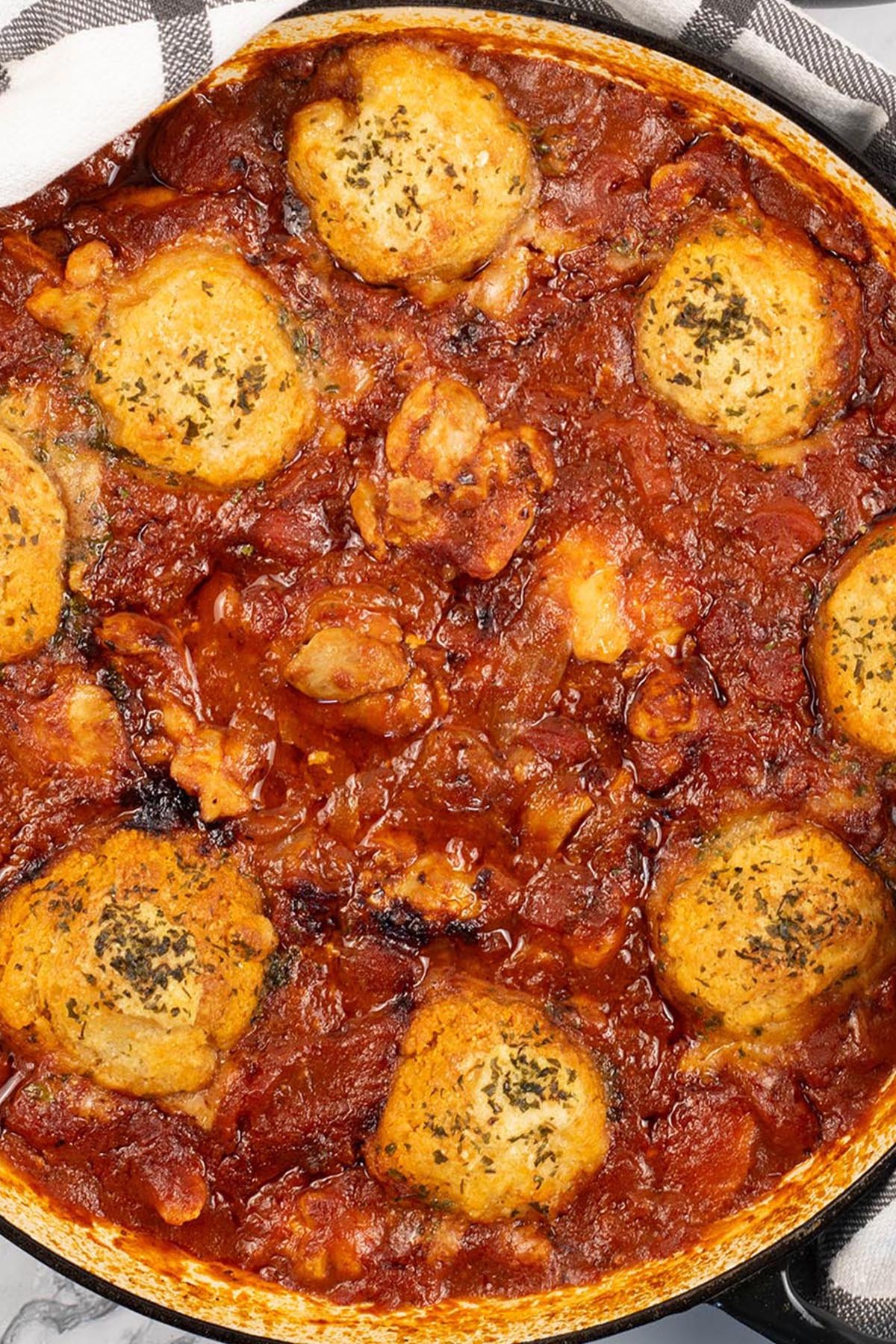 Chicken arrabbiata stew and parmesan dumplings in a shallow round casserole dish.