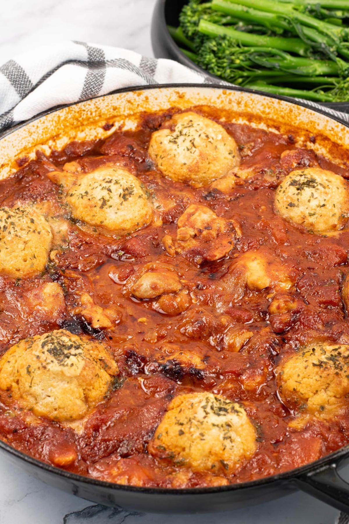 Chicken arrabbiata stew and parmesan dumplings in a shallow round casserole dish with a bowl of tenderstem broccoli on the side.