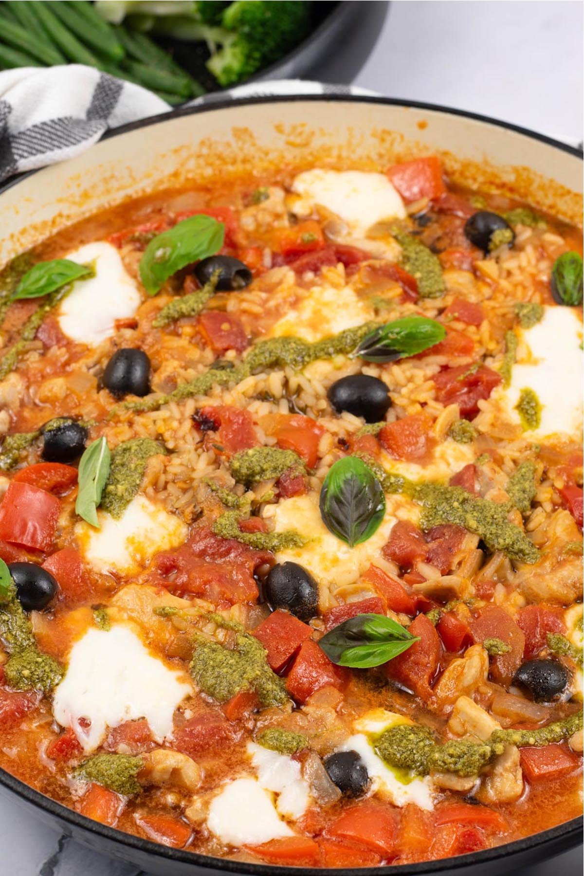Chicken rice with tomato, basil and mozzarella in a large round casserole with a bowl of green beans and broccoli in the background.