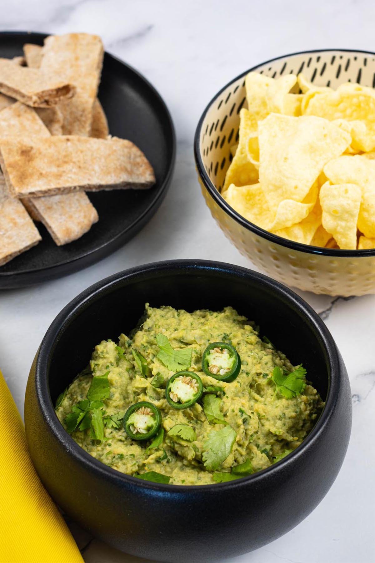 Coriander and green chilli houmous in a black serving bowl garnished with coriander leaves and sliced green chillis.