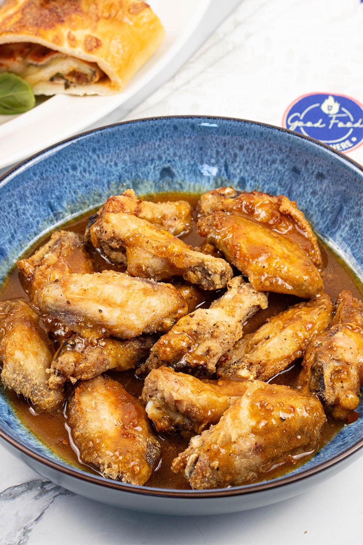 Easy air fryer piri piri chicken wings in a blue patterned serving bowl with a platter of Stromboli on the side.
