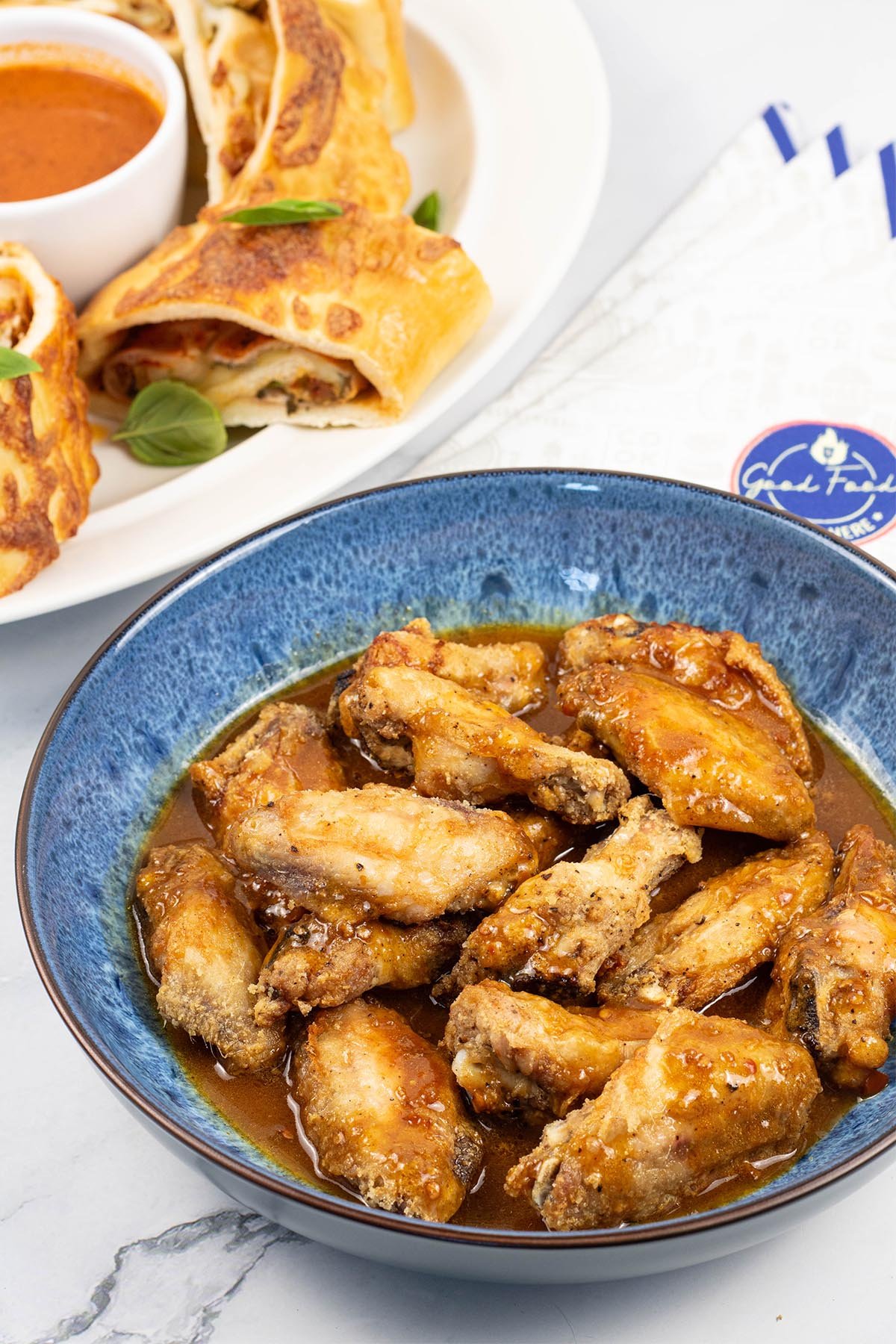 Easy air fryer piri piri chicken wings in a blue patterned serving bowl with a platter of Stromboli on the side.
