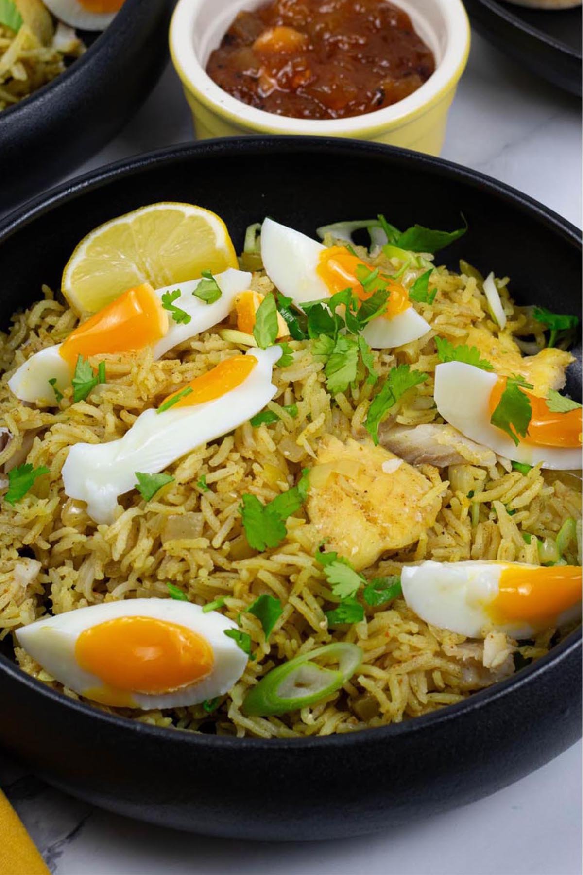 A portion of kedgeree in a black bowl with a small dish of mango chutney on the side.