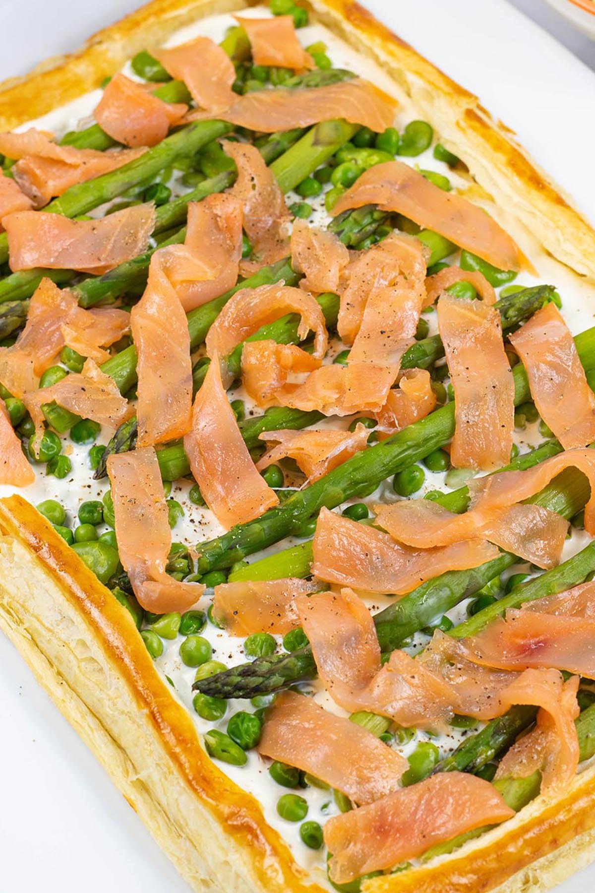 Smoked salmon and spring vegetable tart on a white rectangular serving platter.