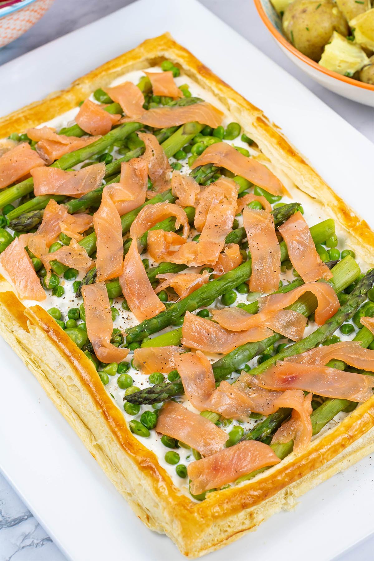 Smoked salmon and spring vegetable tart on a white rectangular serving platter.